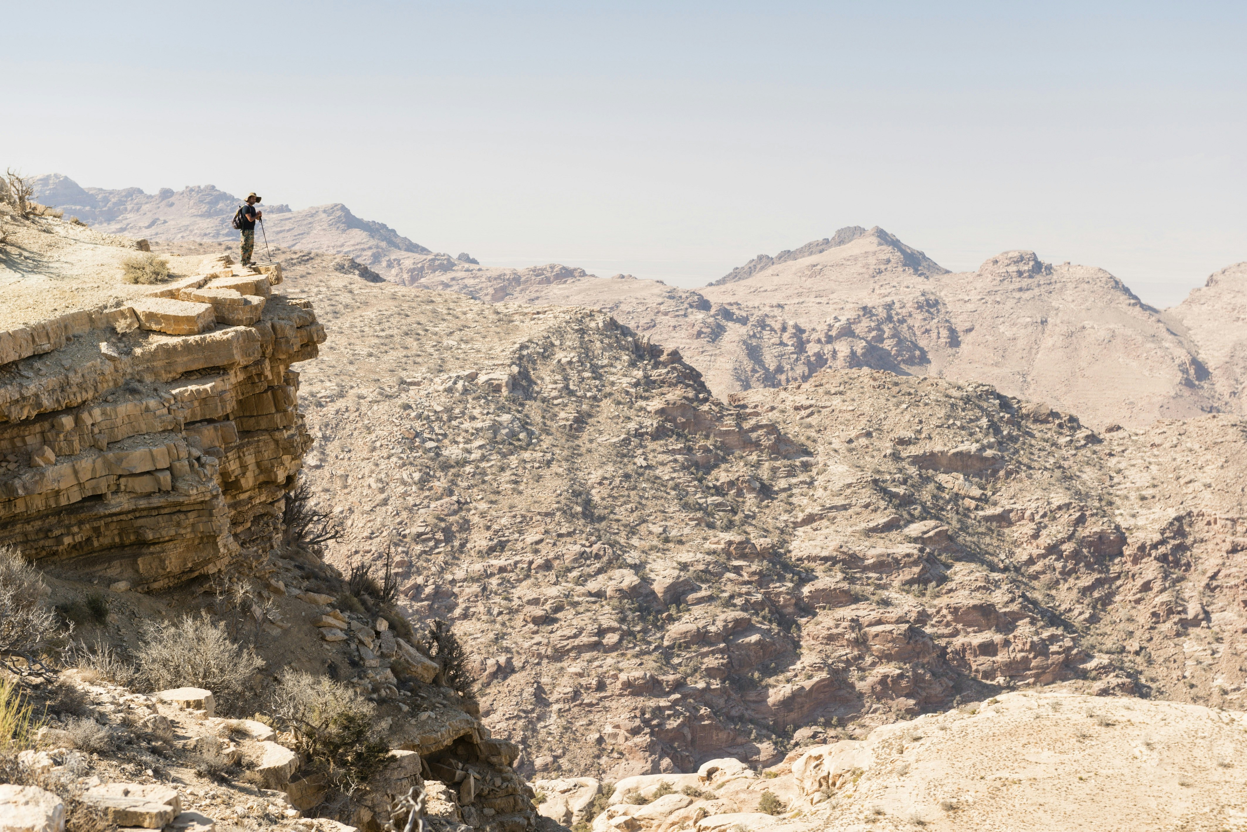 A trekker stands on the edge of a cliff and overlooks a dramatic rocky canyon.