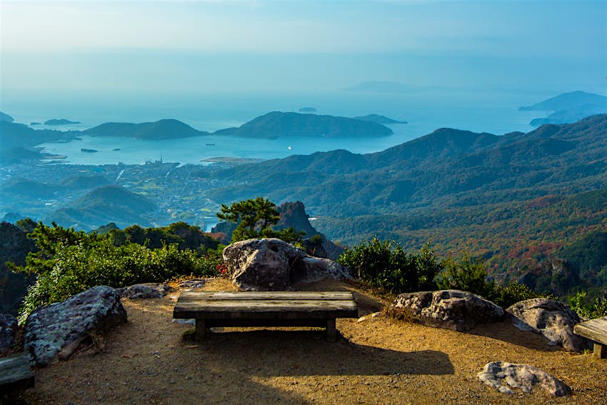 kankakei-gorge-kagawa-japan.jpg A low wooden bench sits empty on an overlook with stellar views of the Kankakei gorge. In the distance, low islands rise out of the denim-colored sea, which blends into the hazy sky