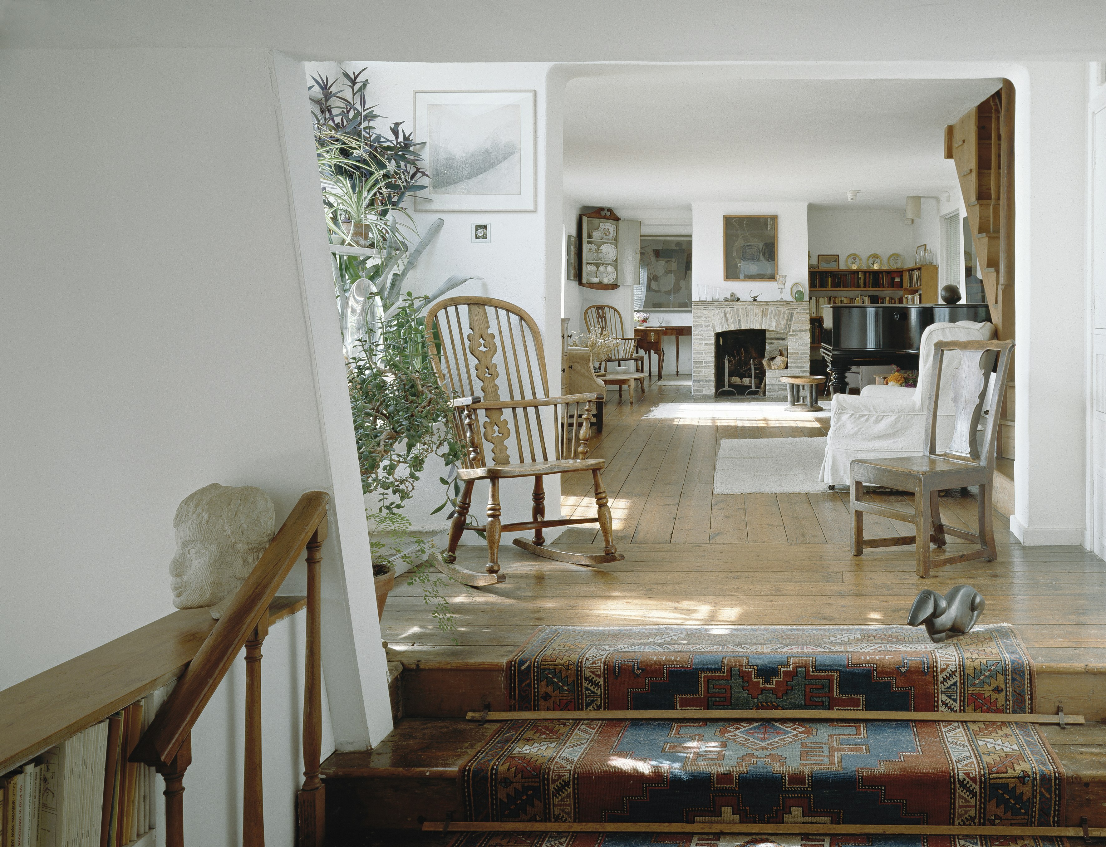 An interior shot of Kettle's Yard, Cambridge. Stairs lead up to a white-walled room furnished like a regular house, but the walls are lined with works from Jim Ede's collection.