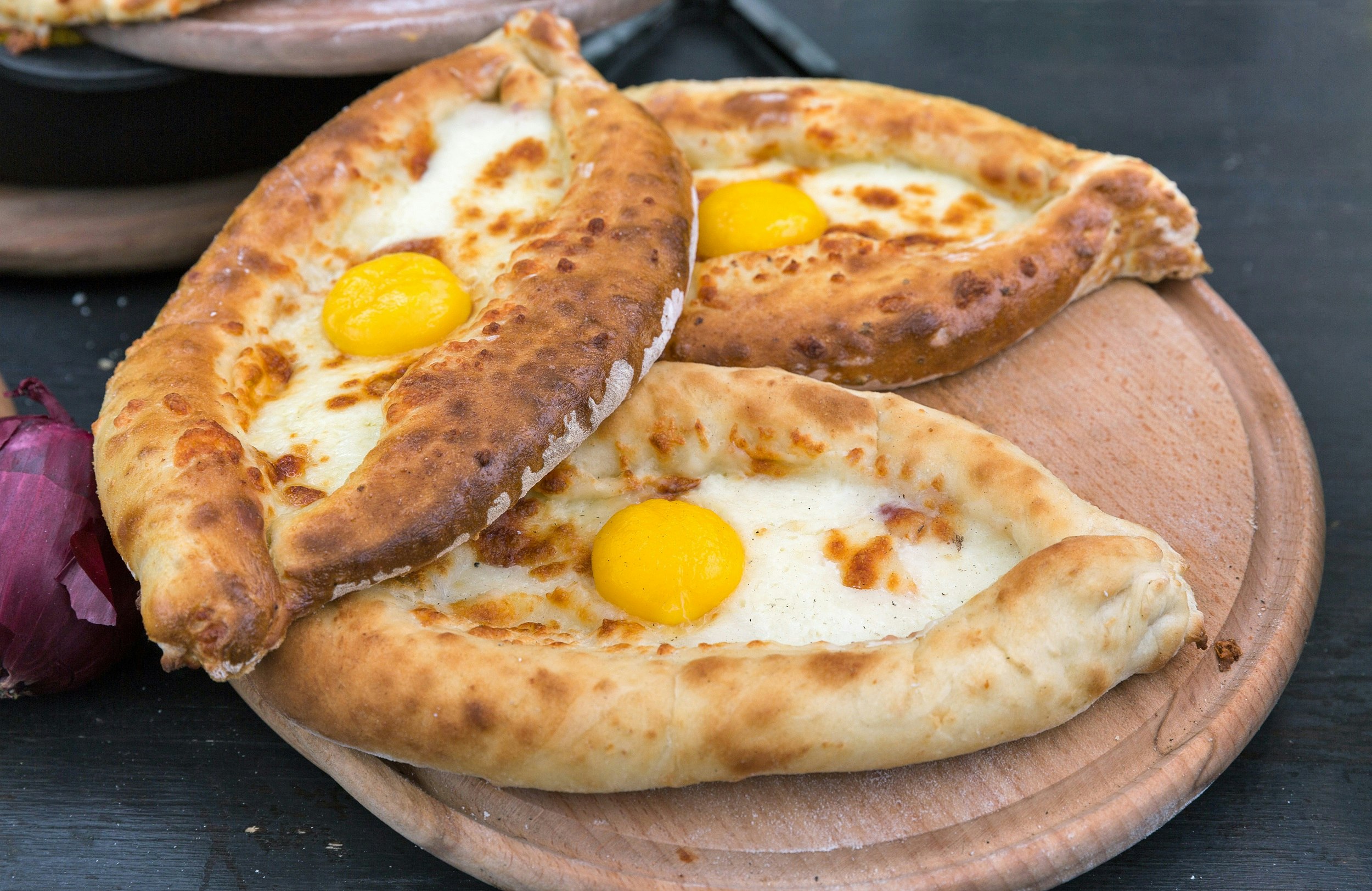 Three boat-shaped pastries with melted cheese and an egg on top
