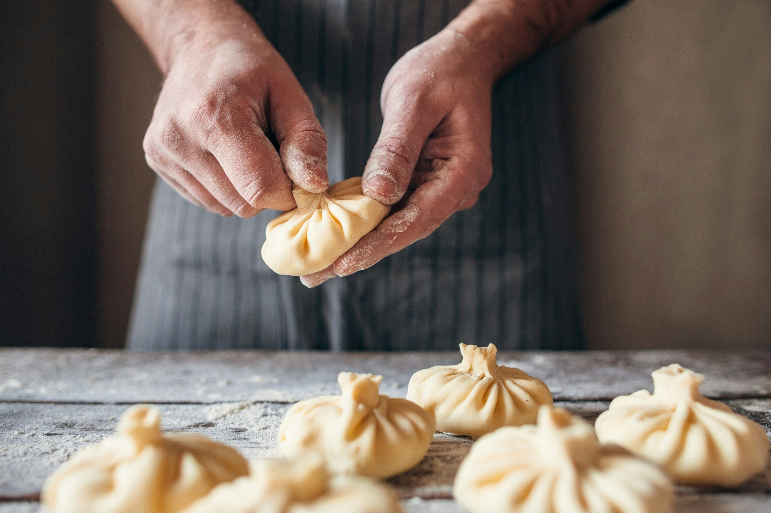 Someone preparing pale dumplings, small parcels of dough pinched together at the top, their hands covered in flour