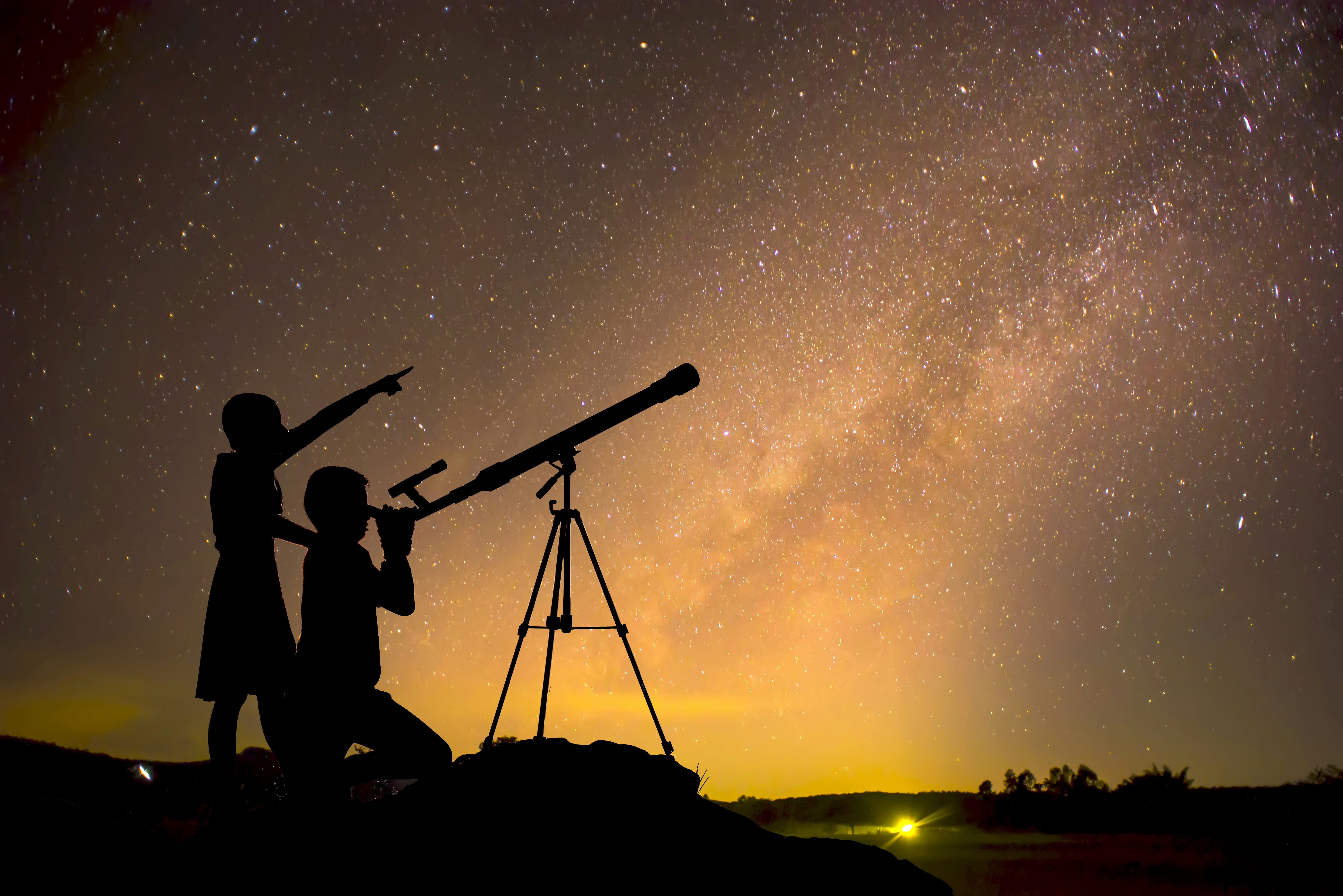 A child peering through a telescope while another points at the sky