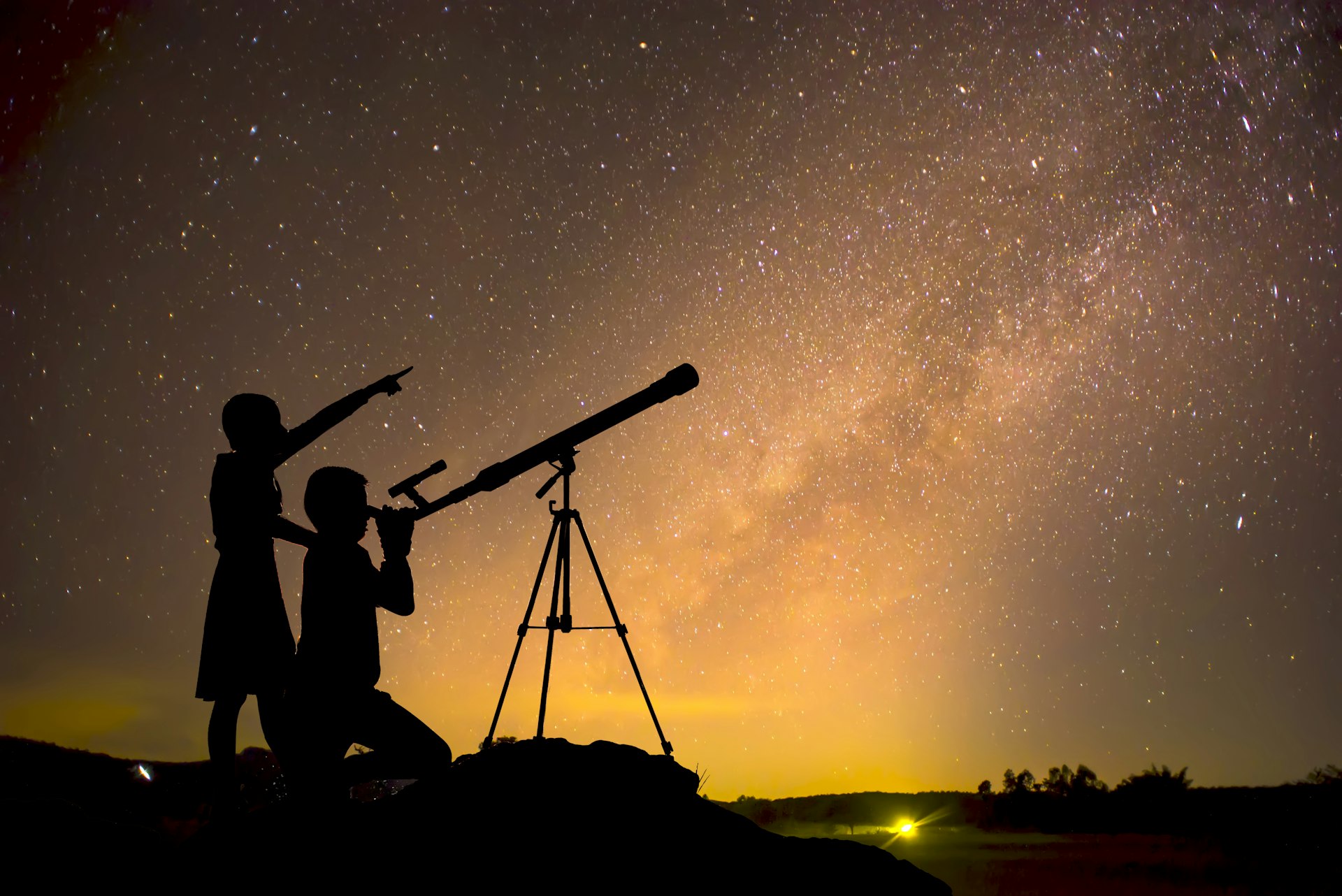 A child peering through a telescope while another points at the sky