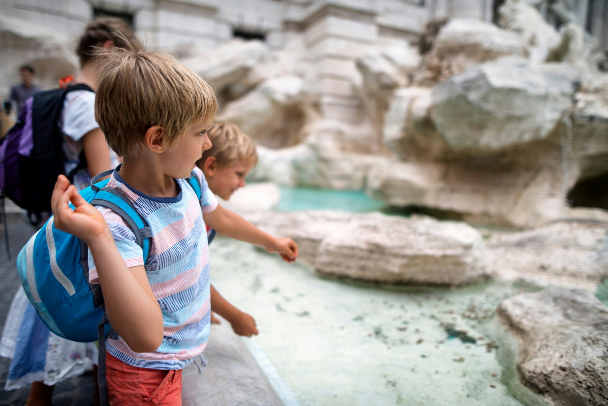 Close-up of kids throwing coins into Trevi Fountain. 
