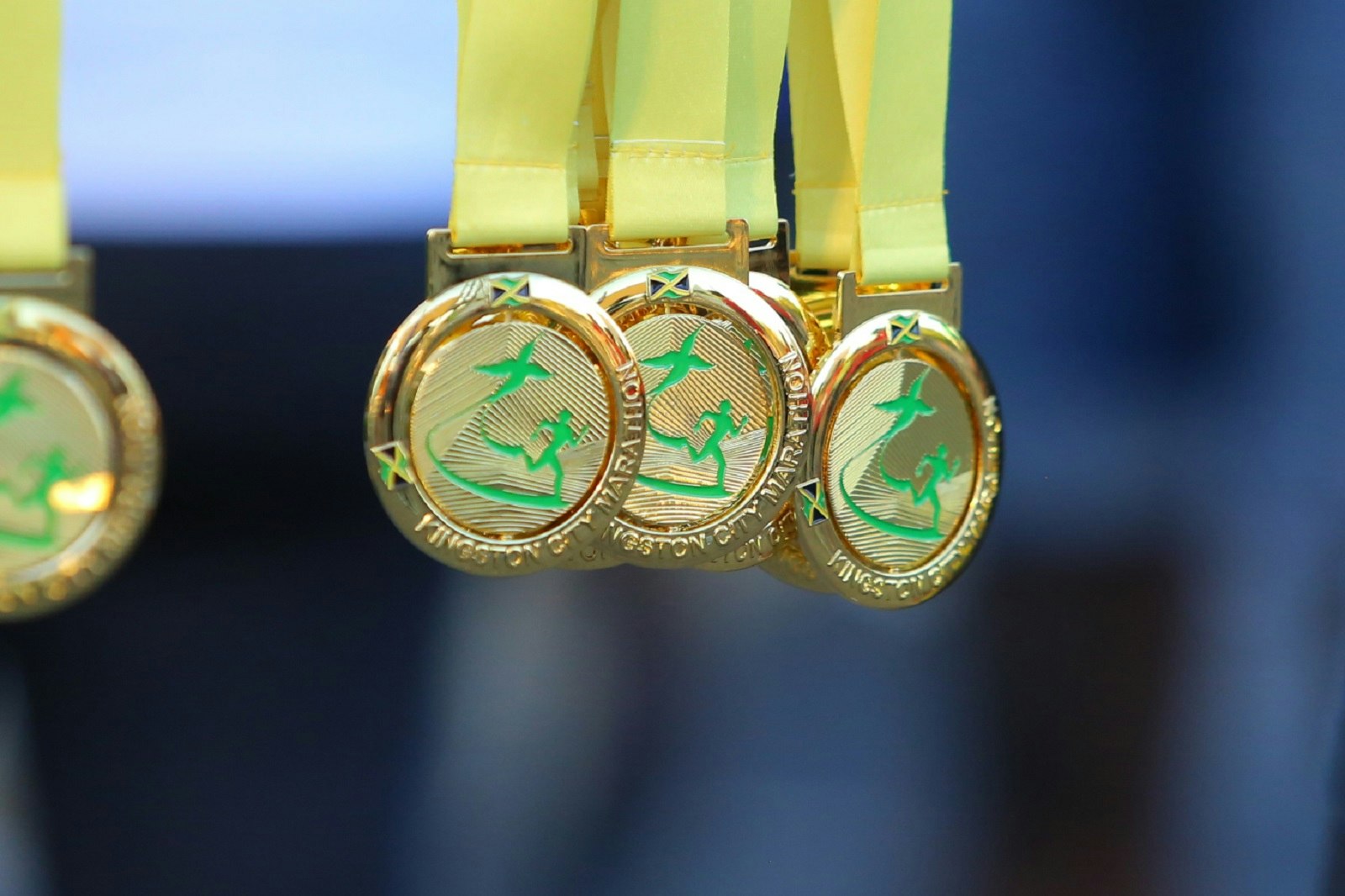 Several gold finishers' medals with gold ribbon hang down with a blurred background; they read 'Kingston City Marathon'
