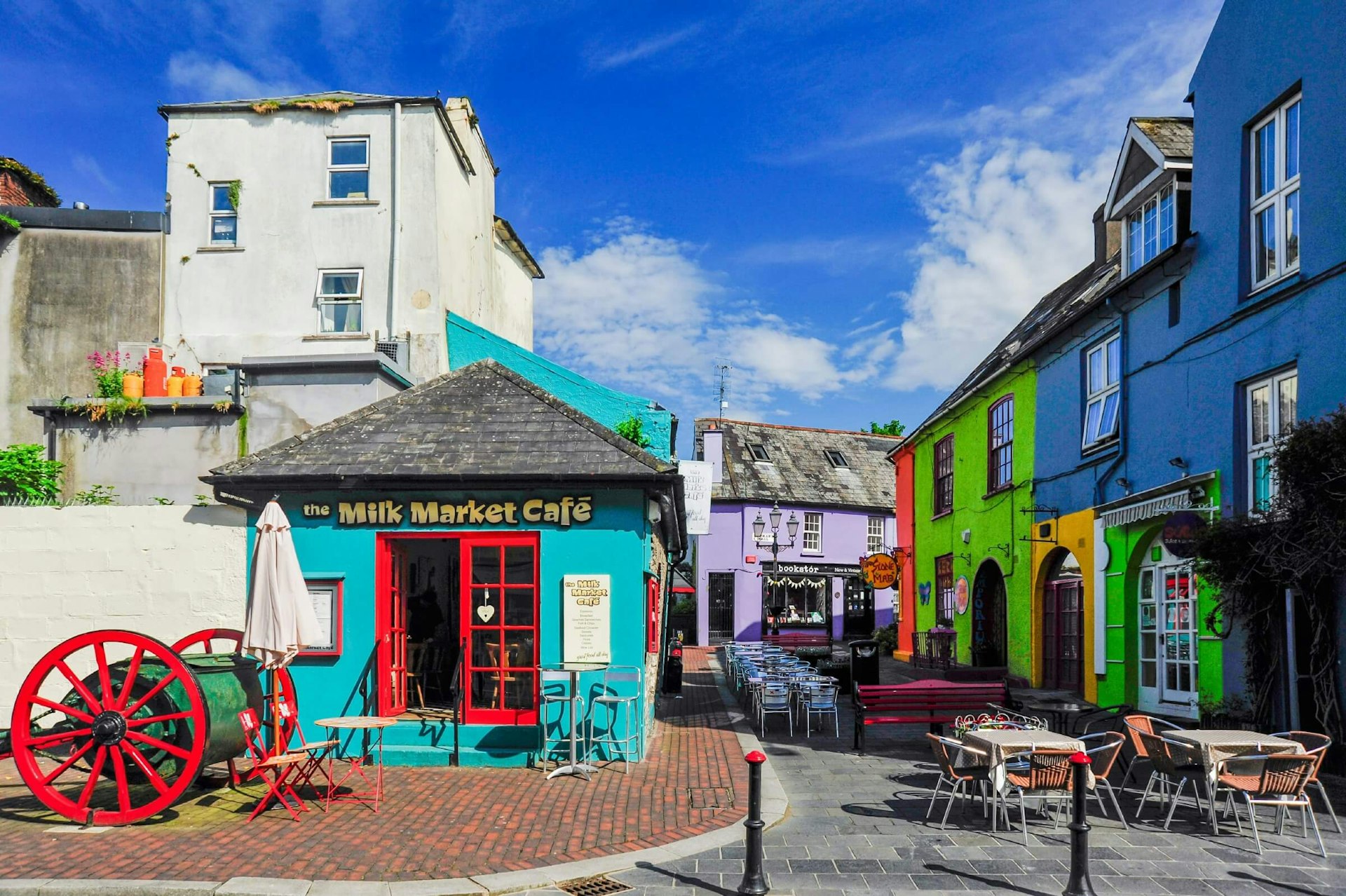 Buildings in Kinsale painted bright colours with table and chairs from a cafe in the foreground