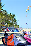 A palm-fringed beach is dotted with kitesurfers preparing their kites on the beach, while many others have already got them airborne.