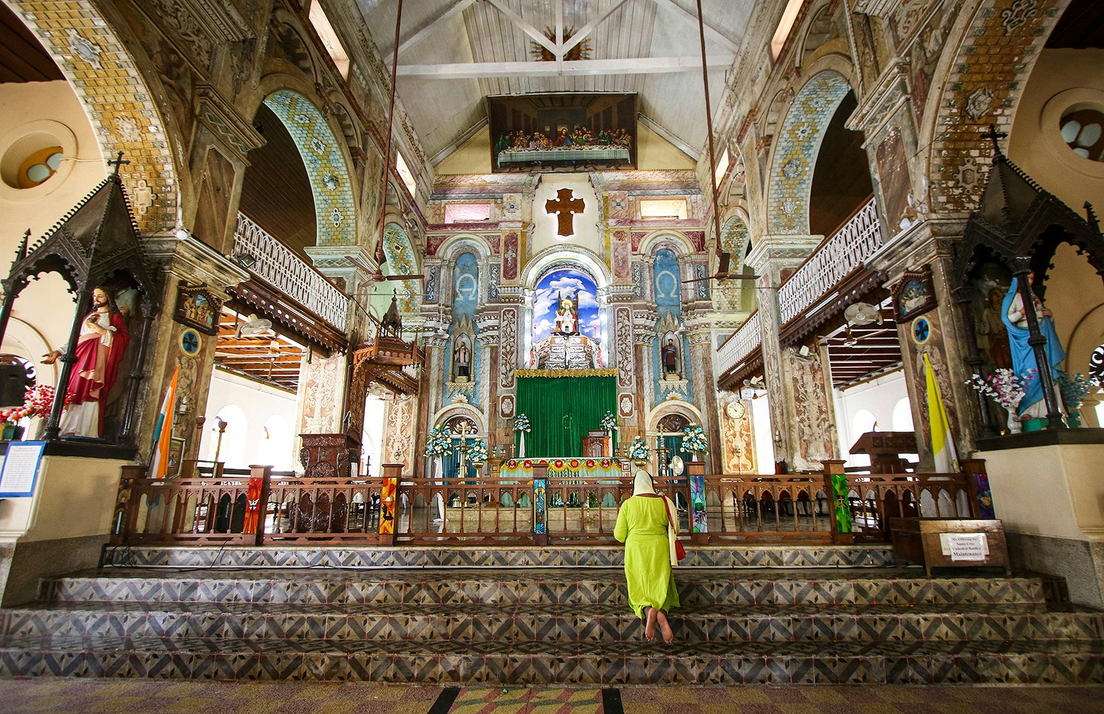 A woman in a chartreuse dress kneels at the alter of the historic St Francis Church in Kochi, India.