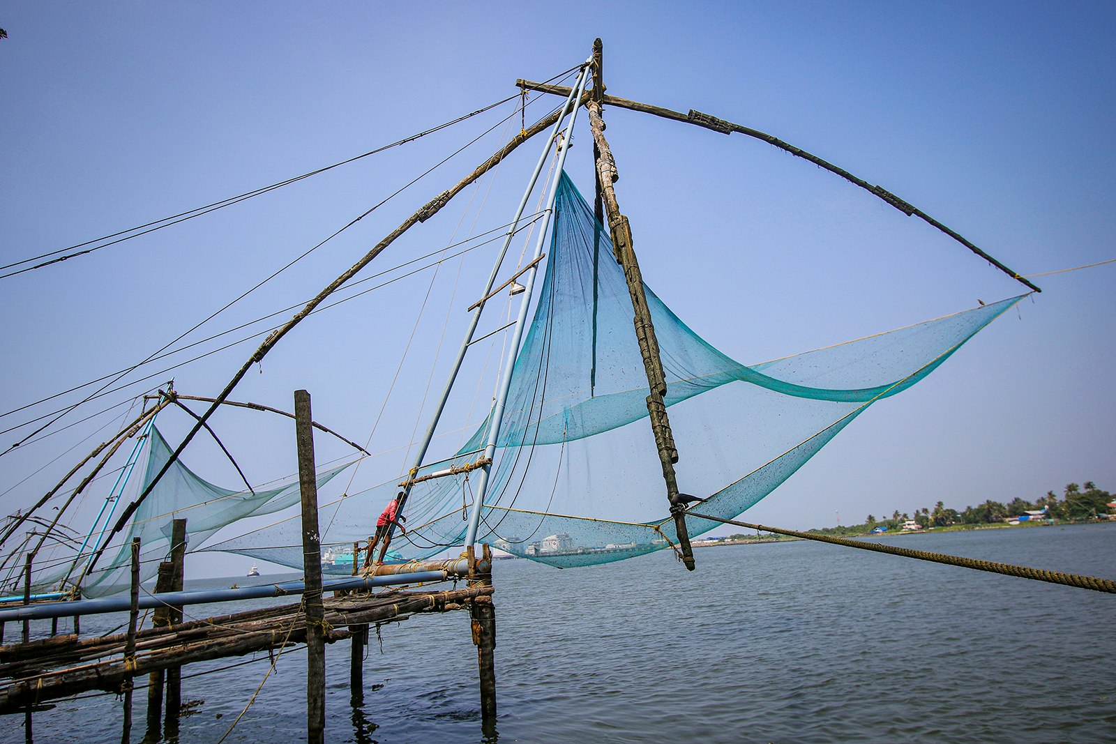 A fisherman in a red shirt operates the large, levered fishing nets of Kochi, India.