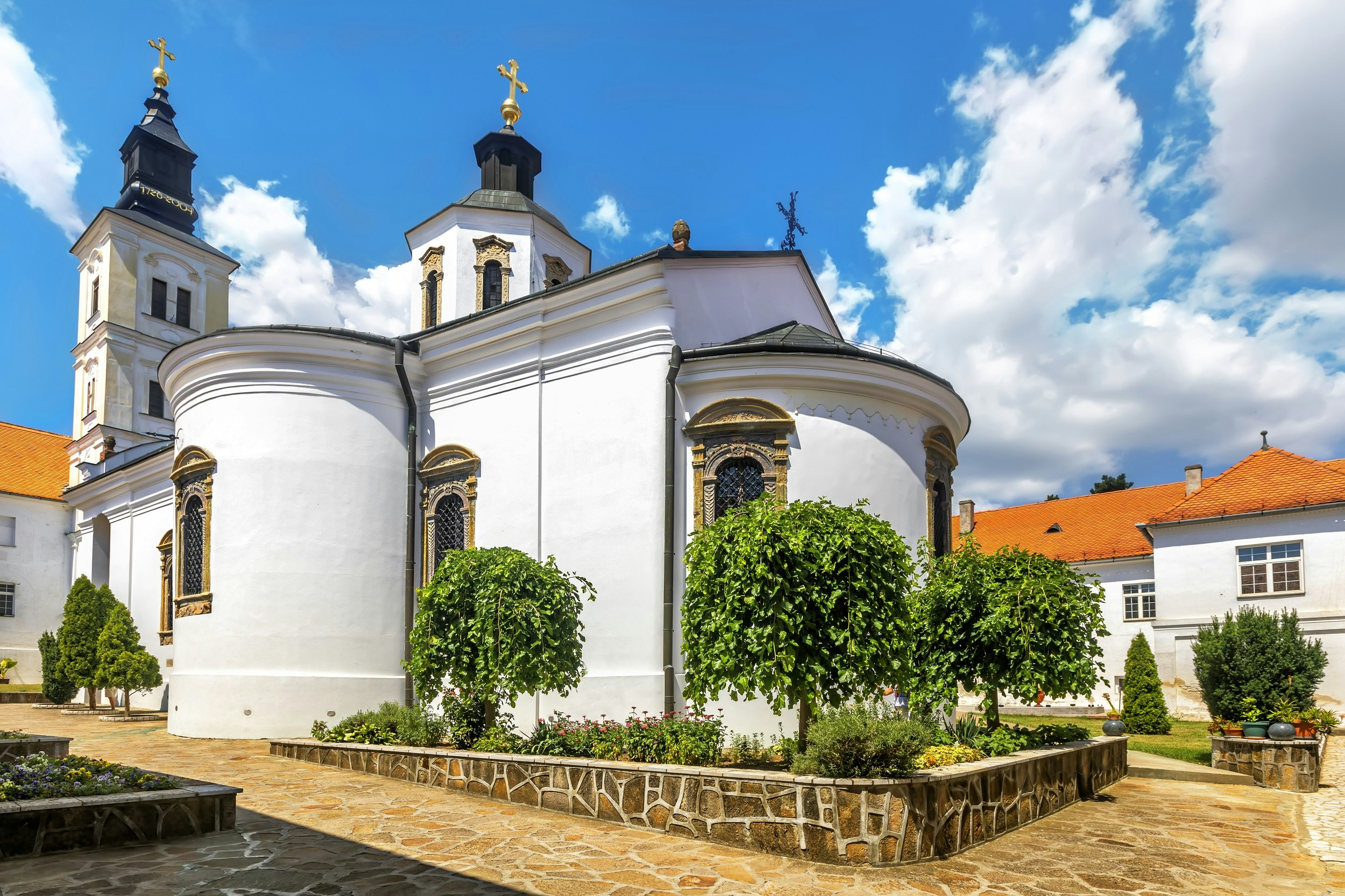 A one-storey white building with a square tower and and hexagonal tower, both topped with gold crosses