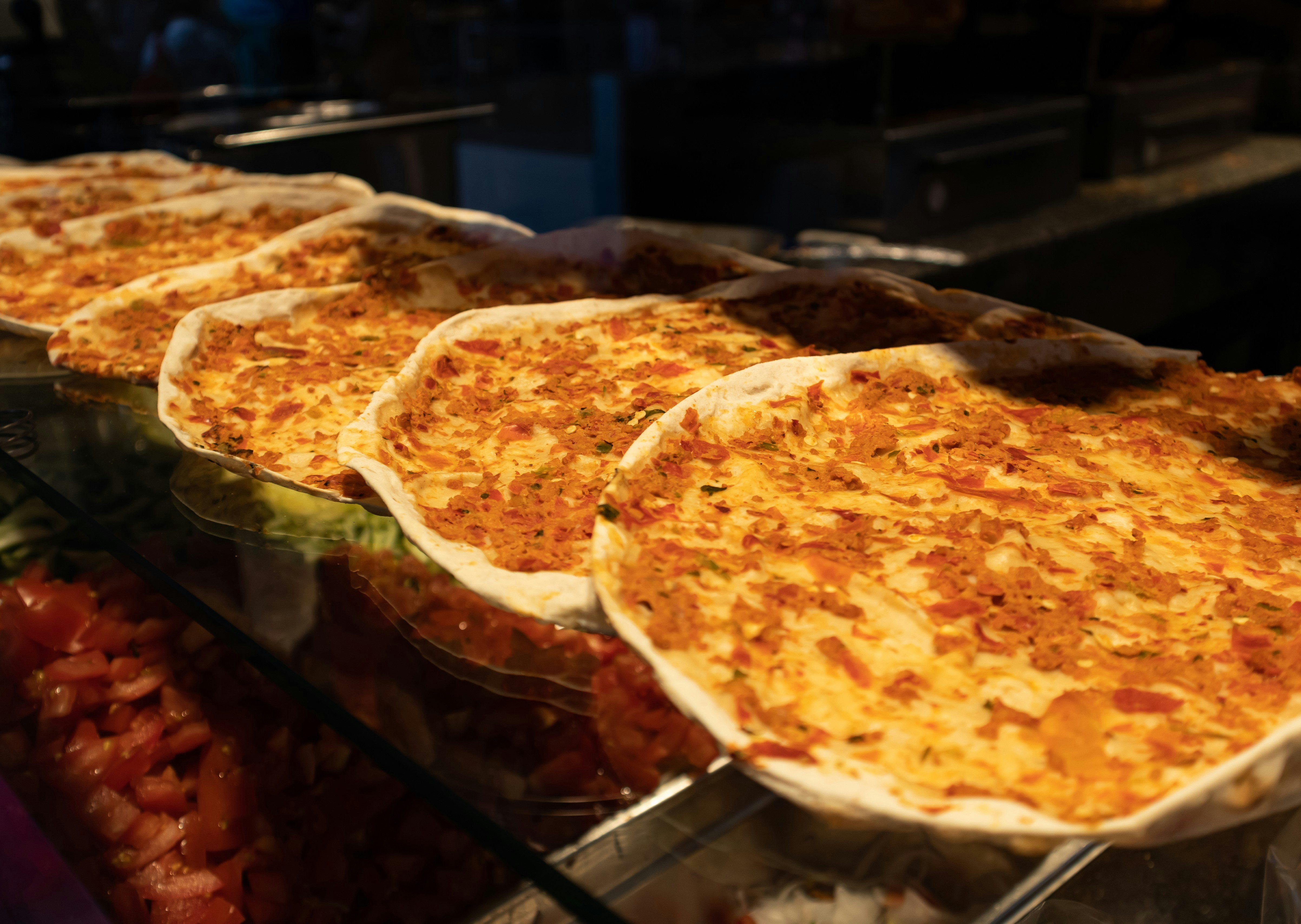 Several lahmacuns on display at a restaurant in the Netherlands. The circular, pizza-like snacks are spread across a glass counter top.