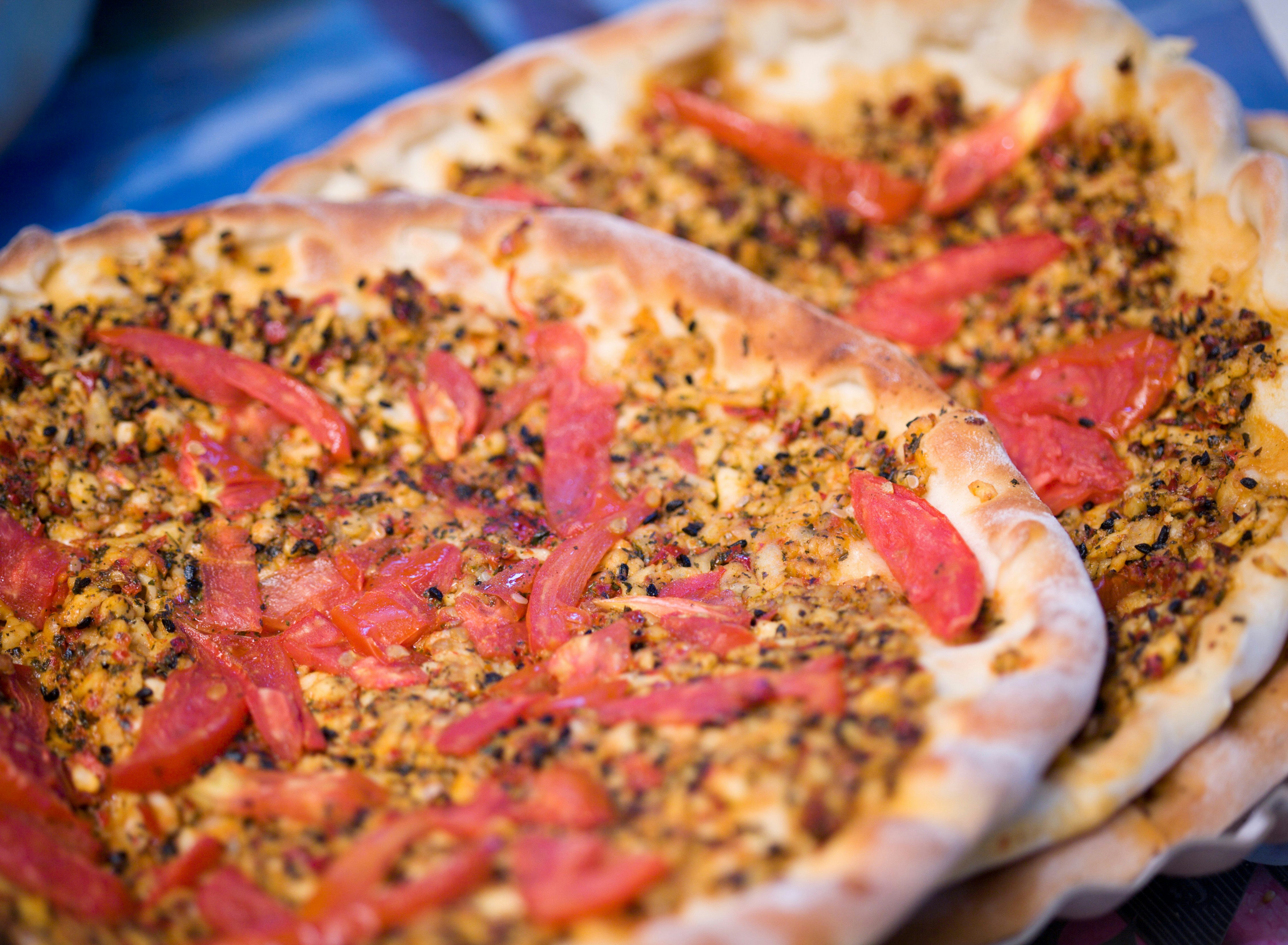 A close-up shot of two lahmacuns: dough that has been rolled into a circular base and baked, then topped with ingredients like chilli flakes and ground meat.