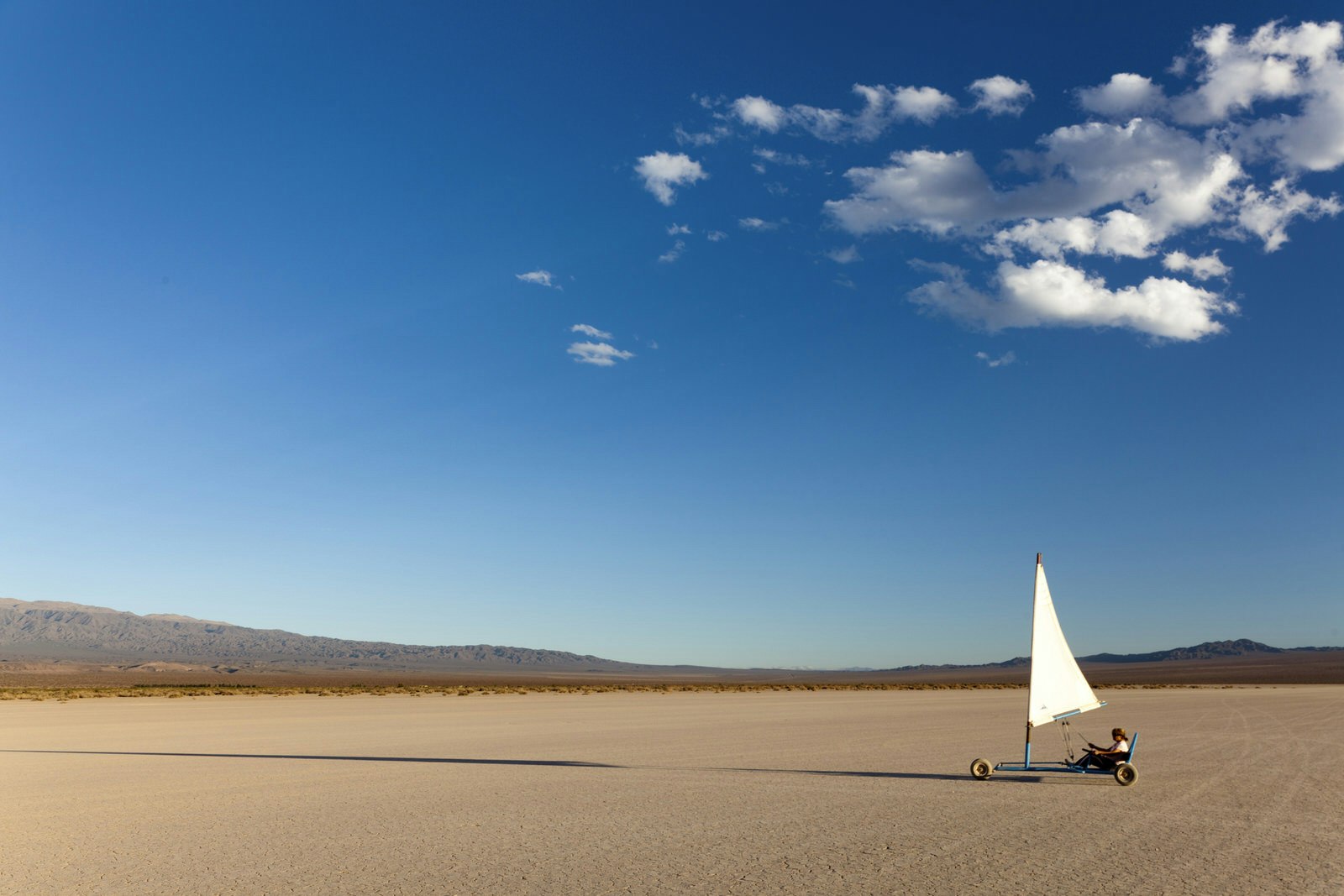 A person land sails across an empty lakebed, with blue skies above.