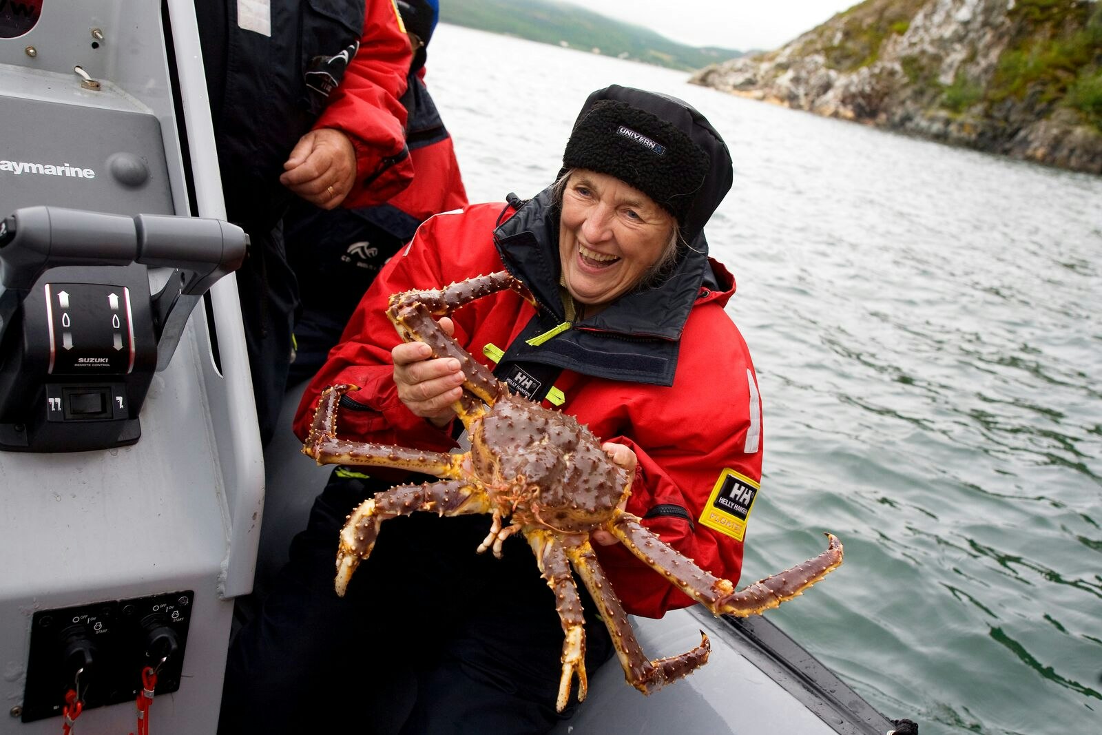 A women in red smiling on a boat holding up a large king crab