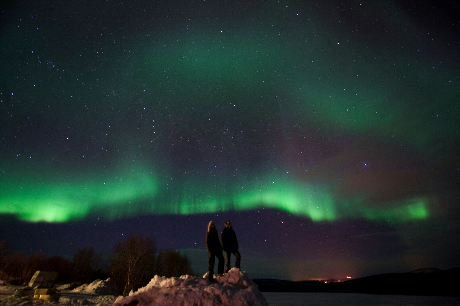 Two people watching the green streaks of the Northern lights across a dark sky