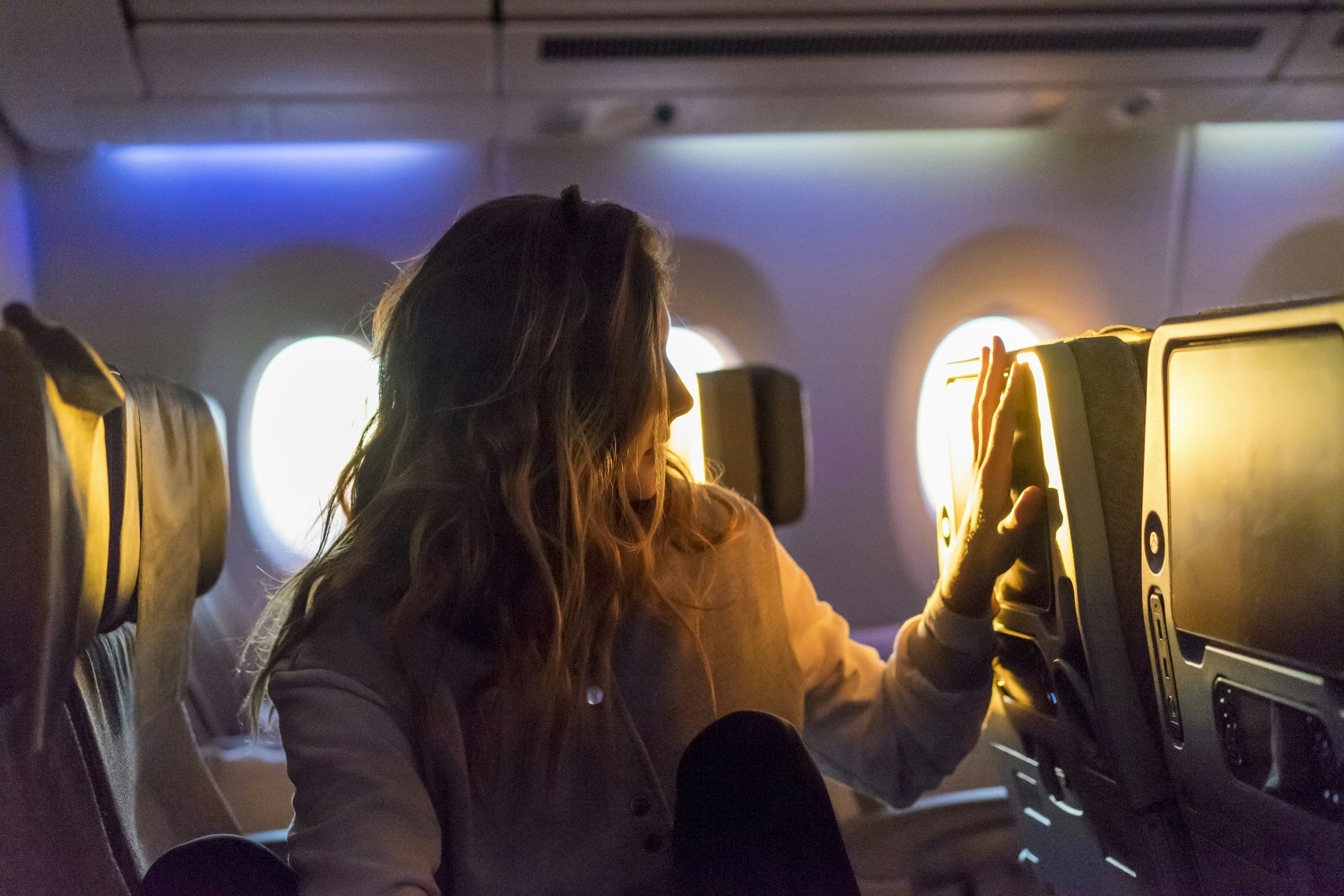 A woman sits in an airplane row bathed in light. 