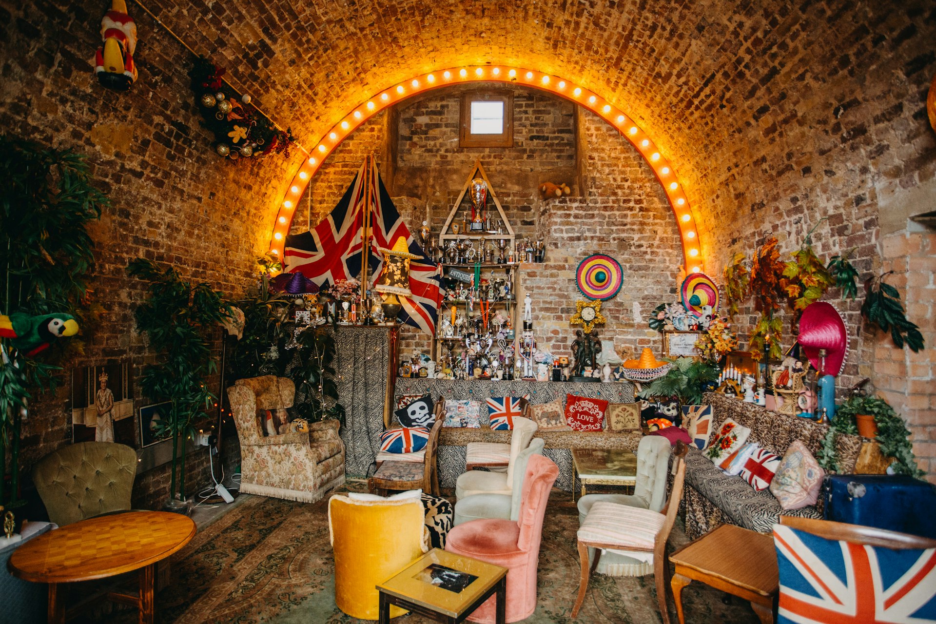 An eccentrically furnished space in a brick arch: it's stuffed with old-fashioned sofas, tables and chairs with flags, knick-knacks and sombreros lining the walls.