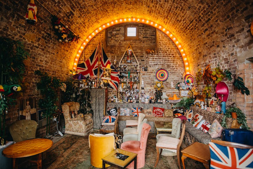 An eccentrically furnished space in a brick arch: it's stuffed with old-fashioned sofas, tables and chairs with flags, knick-knacks and sombreros lining the walls.
