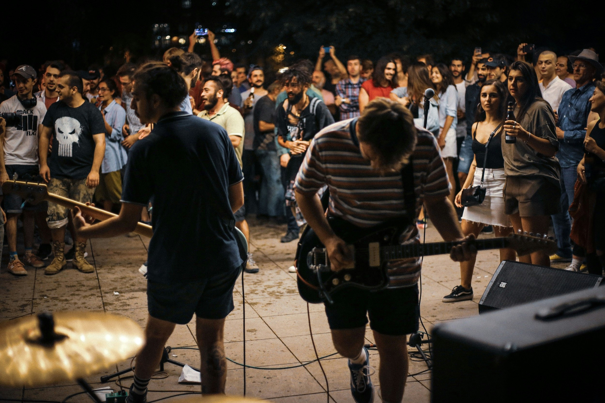 Two guitarists perform to a crowd of people. There's no stage, so the people are gathered around them, creating an intimate vibe.
