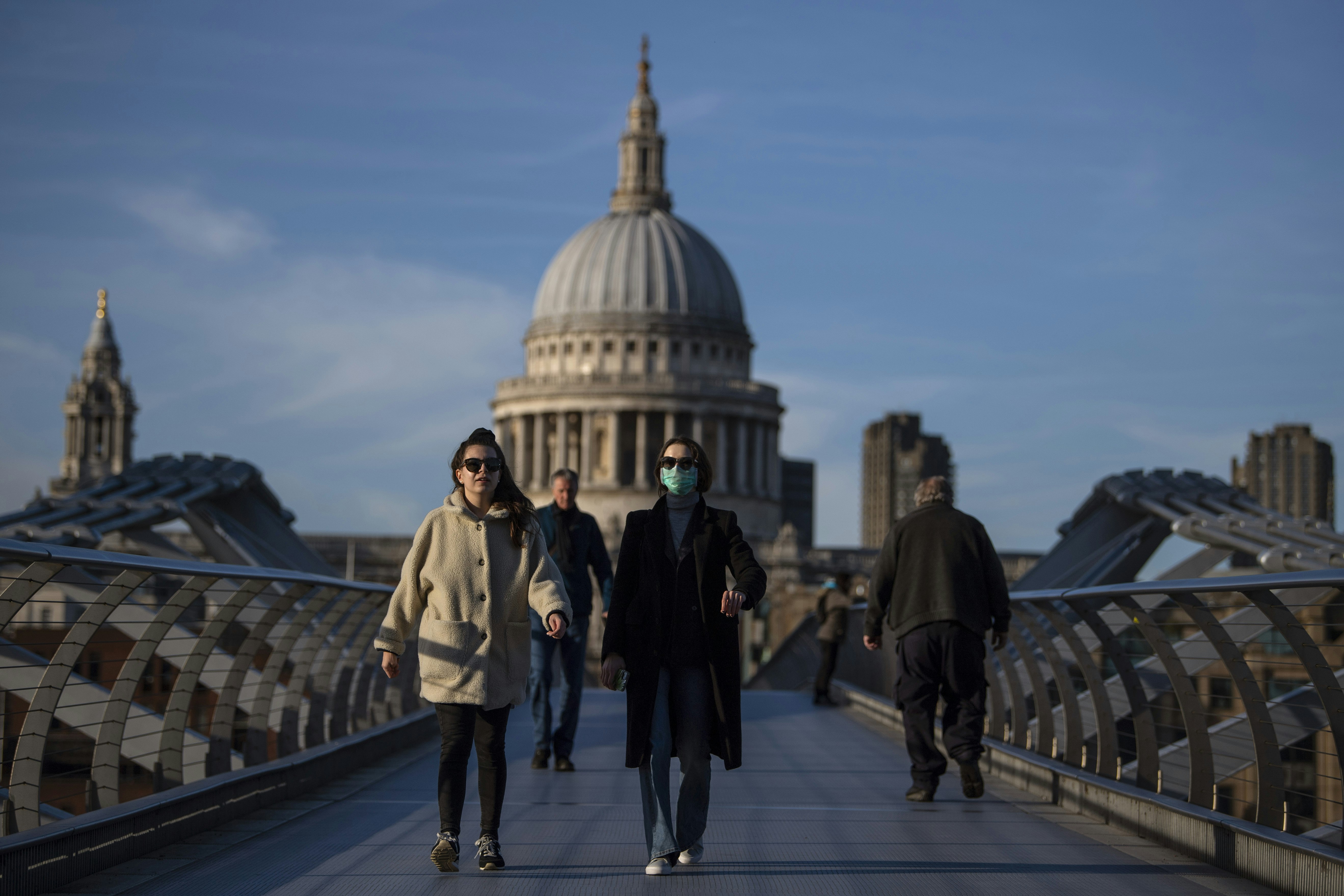 A woman crosses the Millennium Bridge in front of St Paul's Cathedral wearing a face mask during the COVID-19 pandemic in London. 