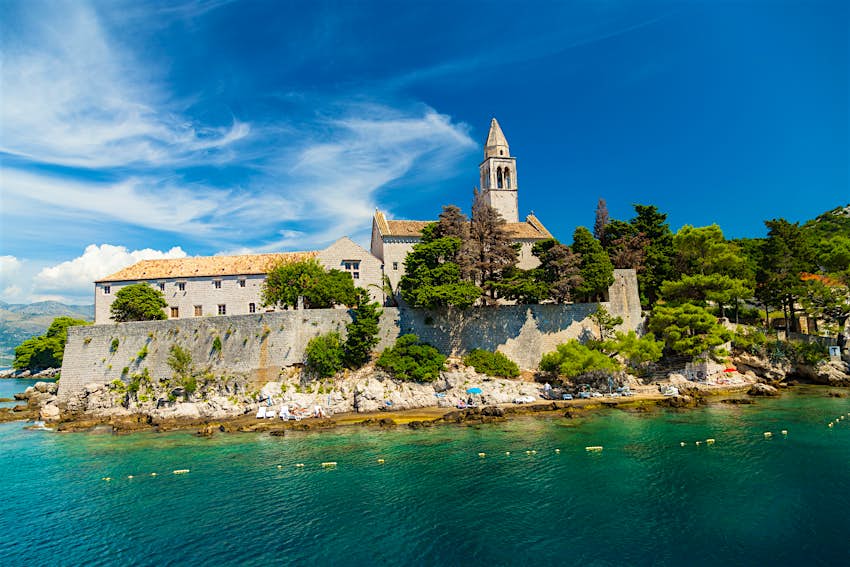 lopud.jpg A stone church and another building behind a defensive wall on a verdant island, with turquoise sea in the foreground.