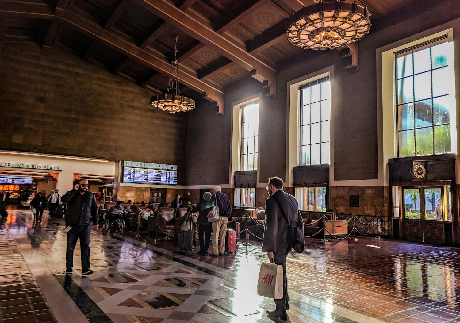 Warm light fills the Mission Revival and art deco interior of Los Angeles' Union Station, which has a dark wood ceiling and dark leather club chairs for passengers to wait in 