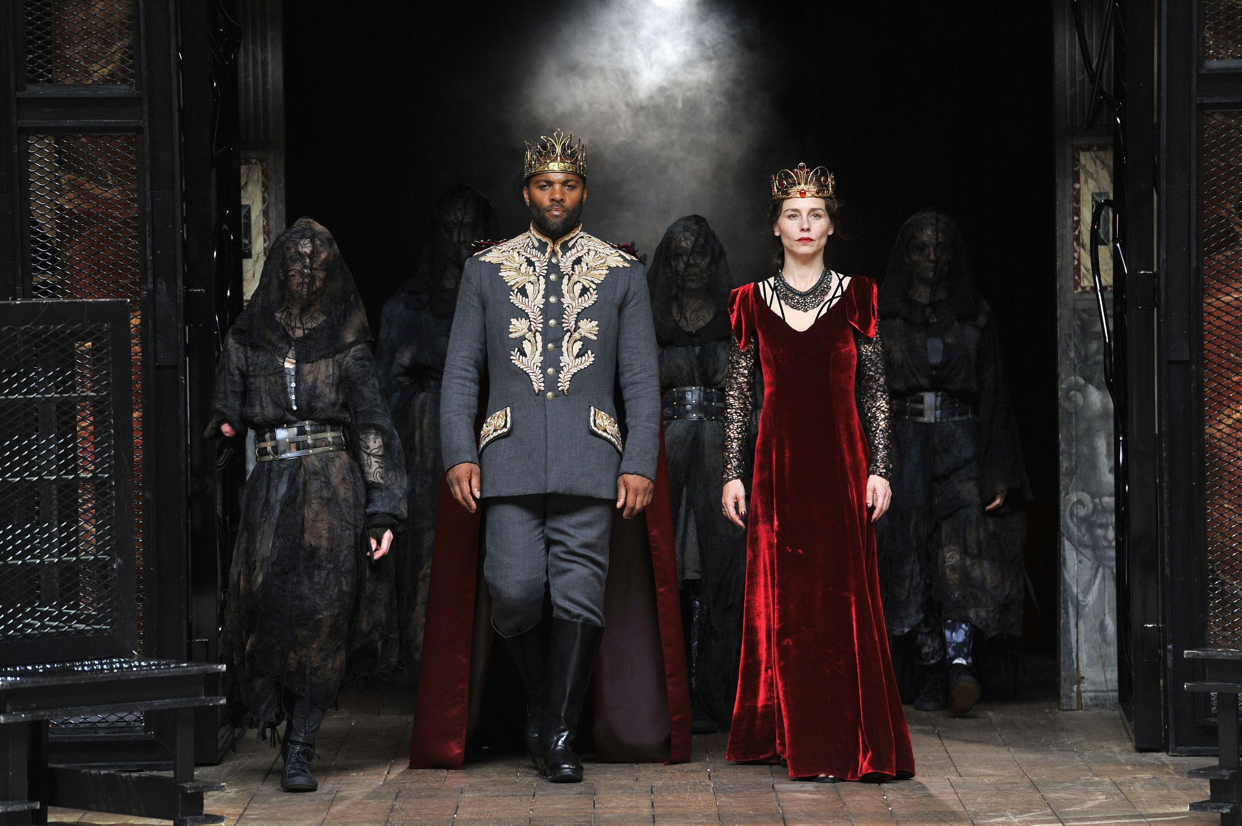 Actors playing Lord and Lady Macbeth in a production at the Globe Theatre walk on stage, in a black suit and red velvet dress respectively