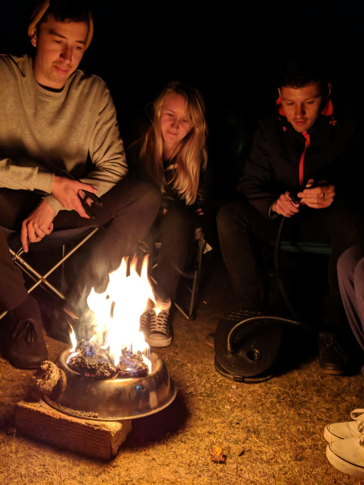 Three people sit around a small fire in a dog bowl, kept away from the ground with blocks of wood. New Forest spending diary