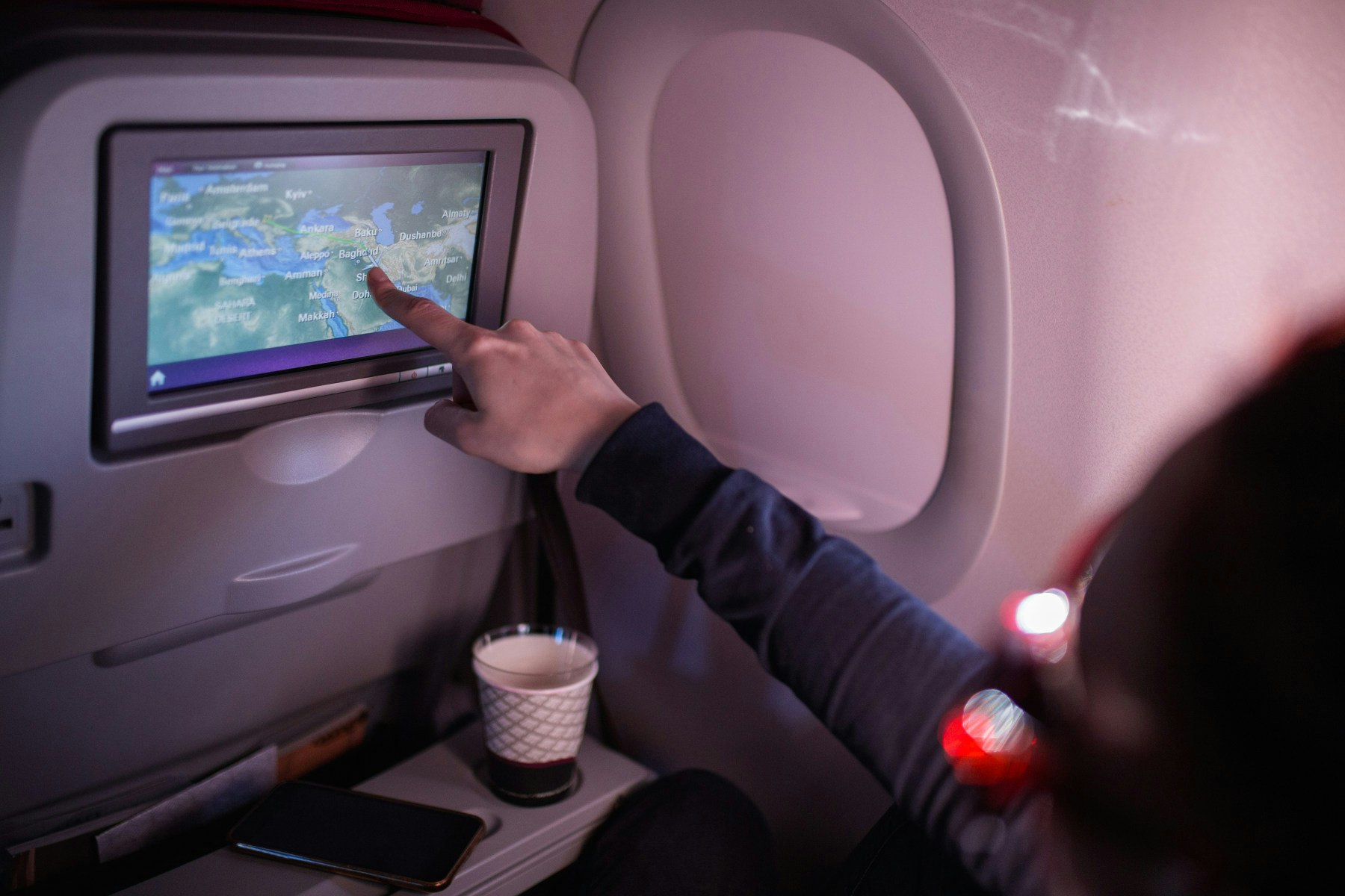 A finger comes up to touch the interactive map on an airplane screen.