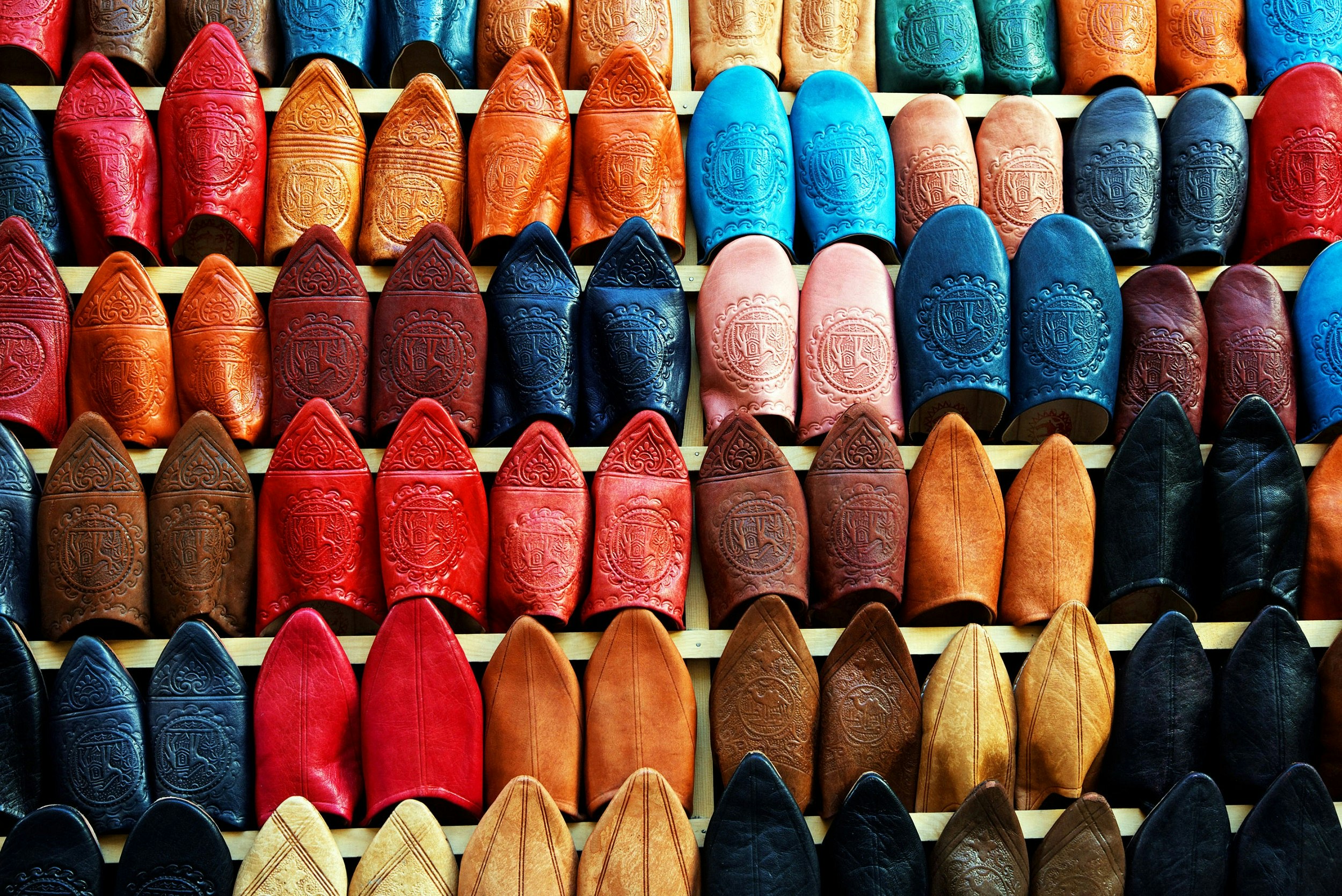 The entire shot is filled with a wall covered in traditional Moroccan slippers; they are all hanging vertically, with the colourful toe of each slipper being visible.