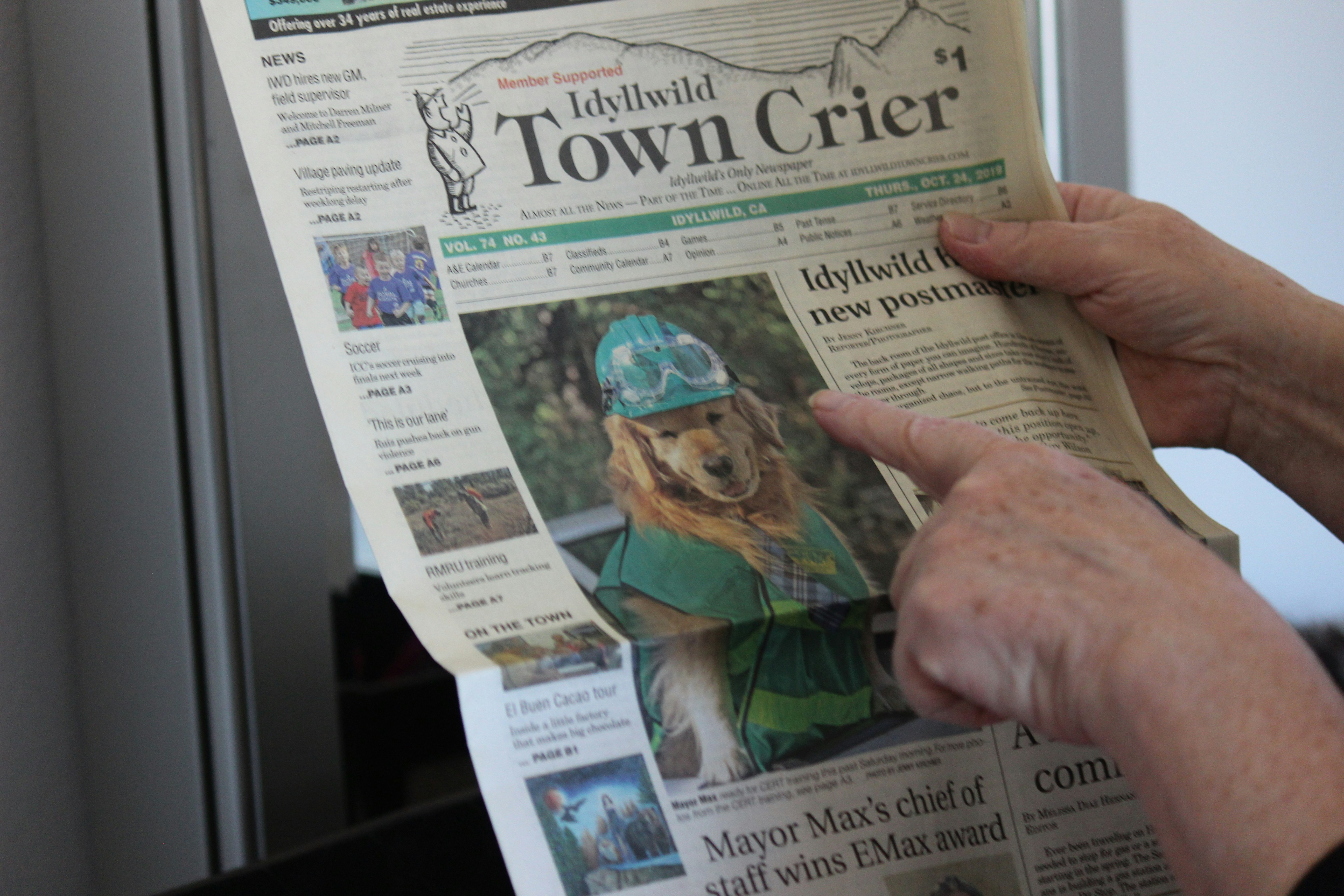 A hand points to a local newspaper with a dog featured above the fold