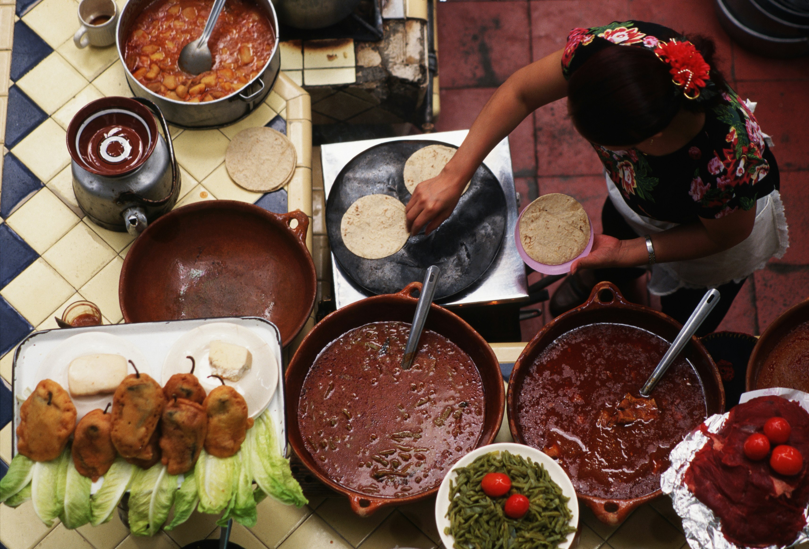 View looking down on a woman preparing food at a stall in Mercado Libertad. There are large saucepans filled with on the counter.  