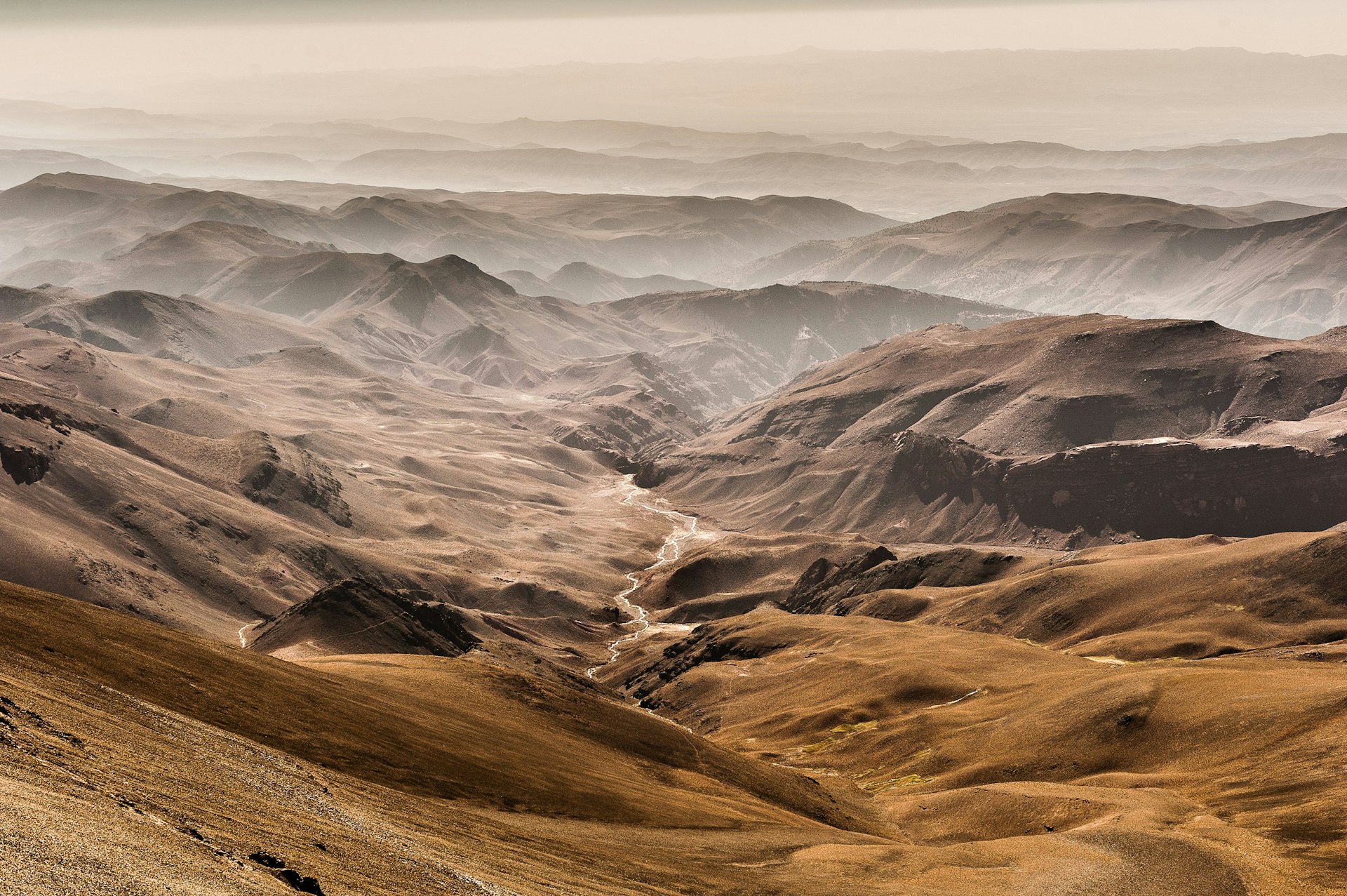 A view down over the desert-like foothills of the High Atlas Mountains; streams meander and low mist hangs in the lower valleys.