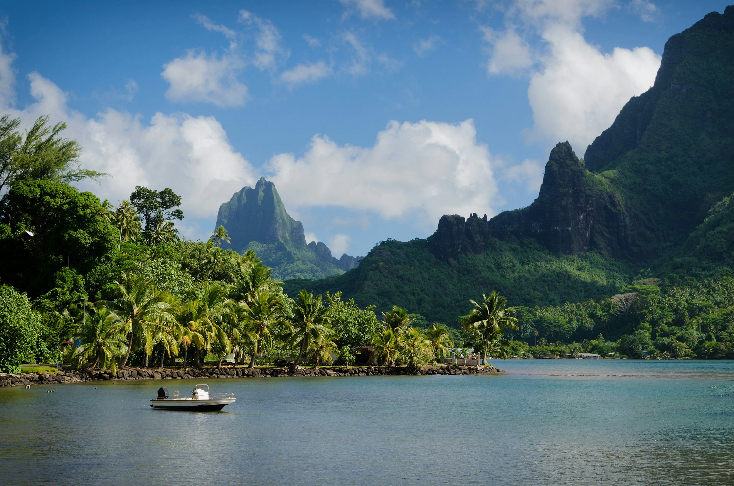 The tropical-forest-covered peaks of Mo'orea Island; a small boat is stationary in the water just off the shore.