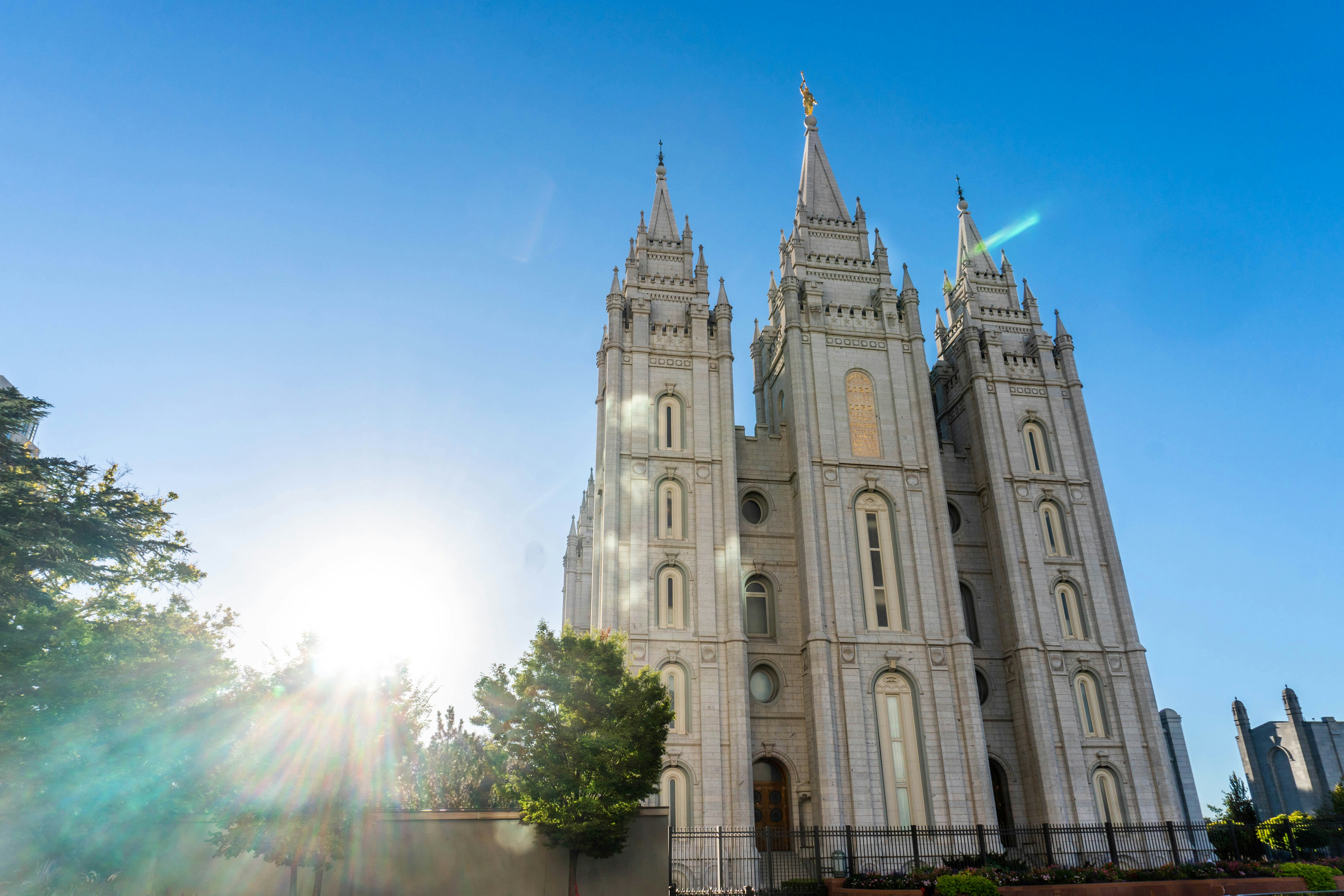 Exterior of the Salt Lake Temple at Temple Square, with a shining sun and blue skies overhead