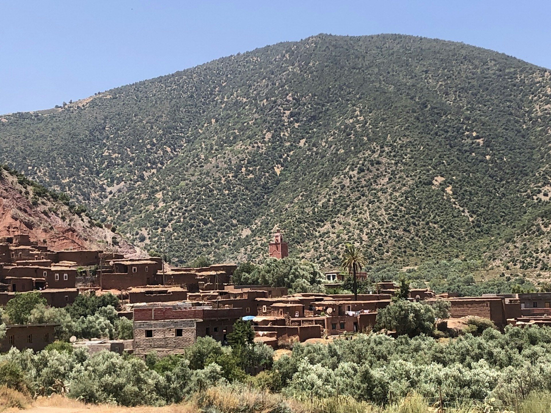 A mud-brick village sits nestled amongst scrub vegetation in the foothills of the Atlas Mountains.