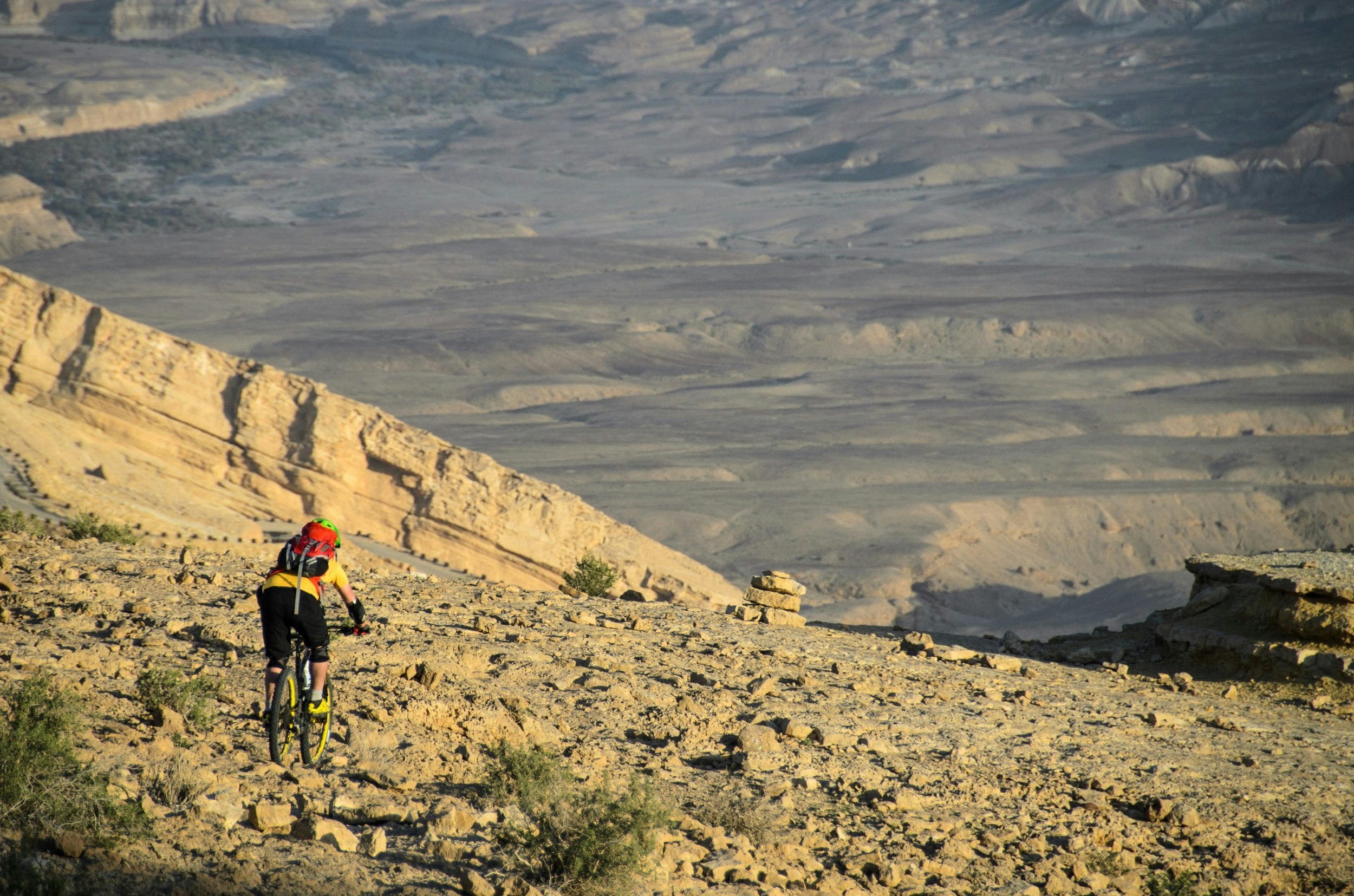 A lone mountain biker gets ready to descend from a mountain to the desert floor far below.