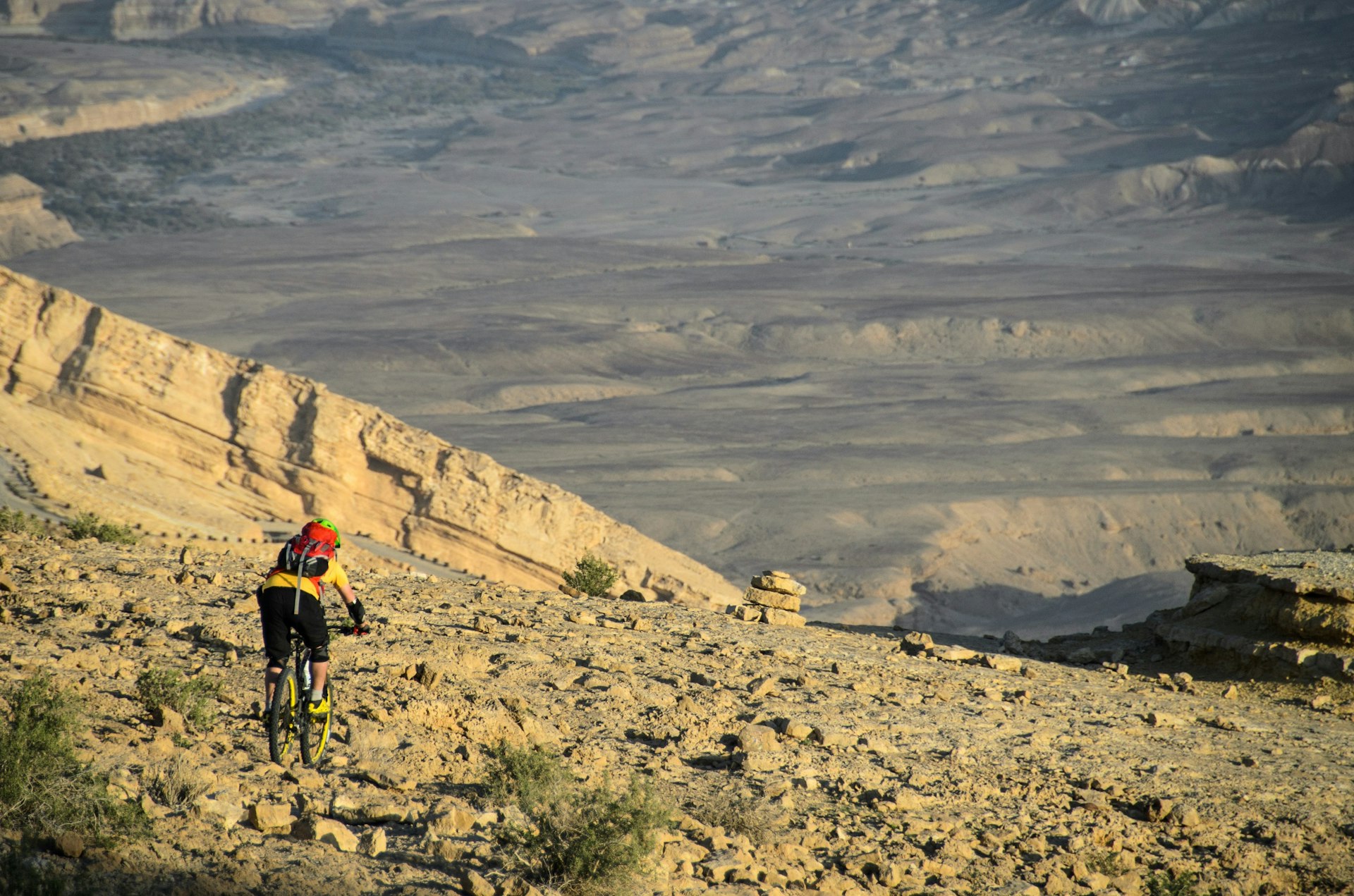 A lone mountain biker gets ready to descend from a mountain to the desert floor far below.