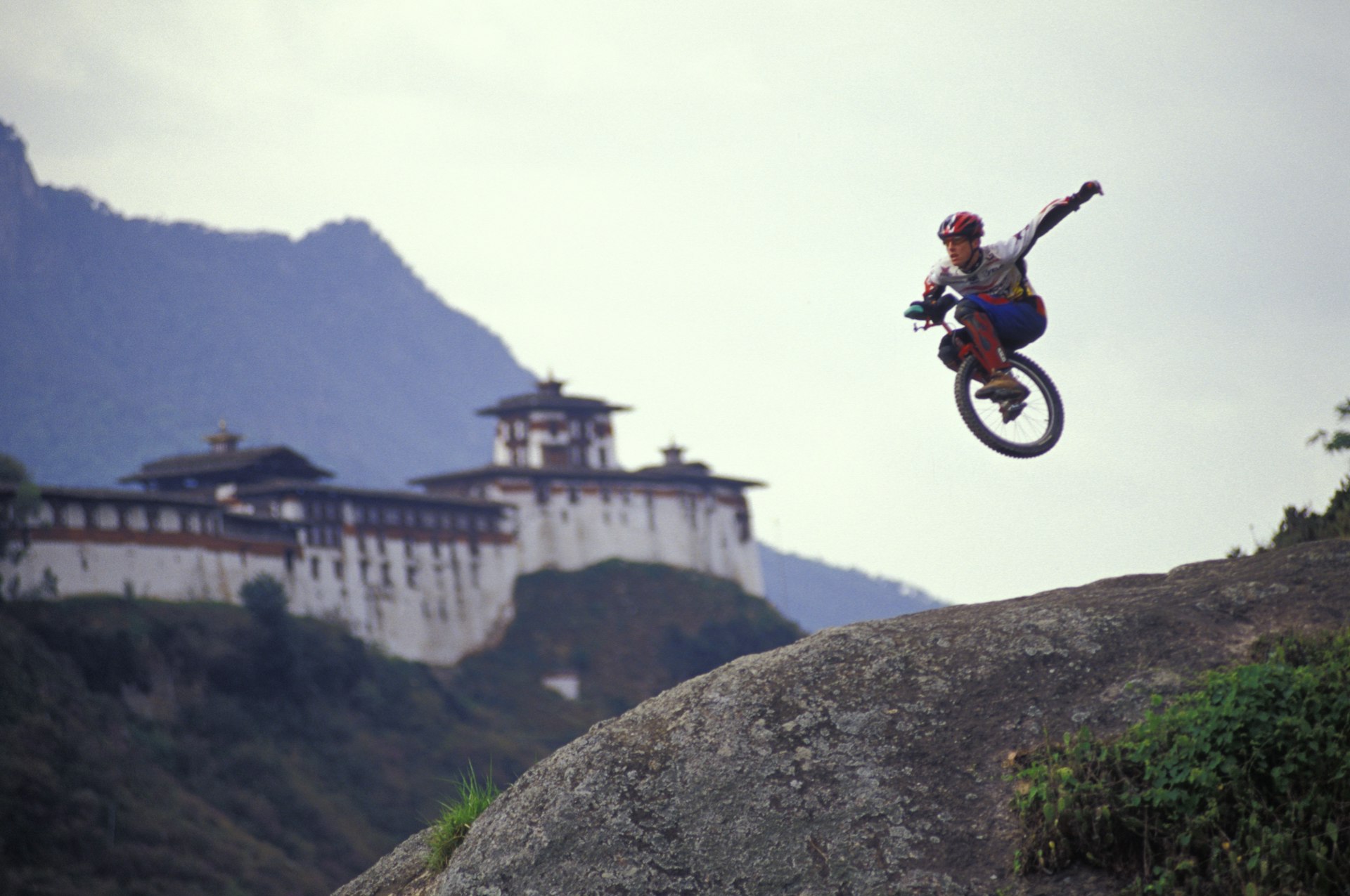 A uni-cyclist flies through the air with a traditional temple fortress in the background.