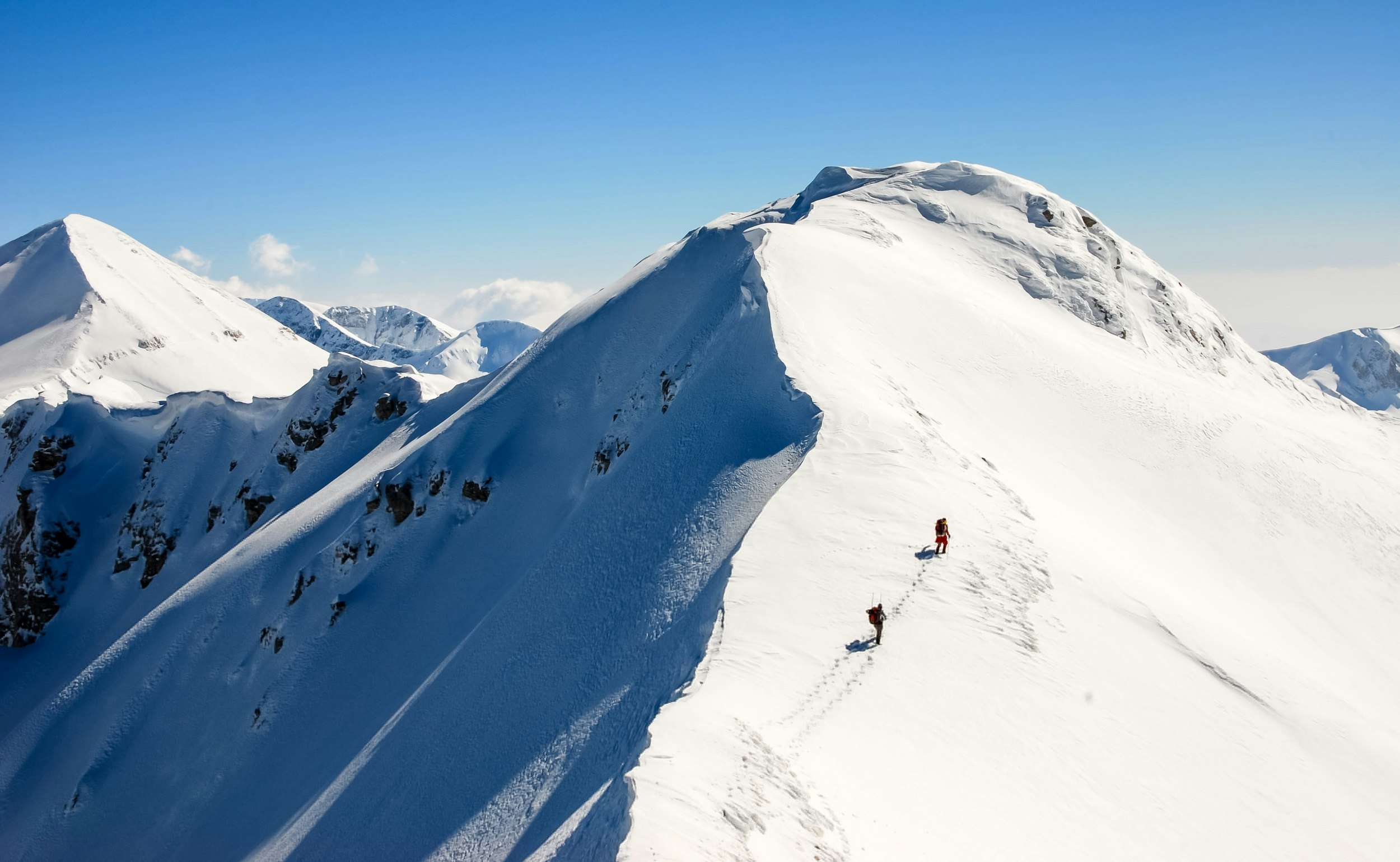 Two trekkers on a sharp, snowy mountain ridge within the Pirin Mountains of Bulgaria.