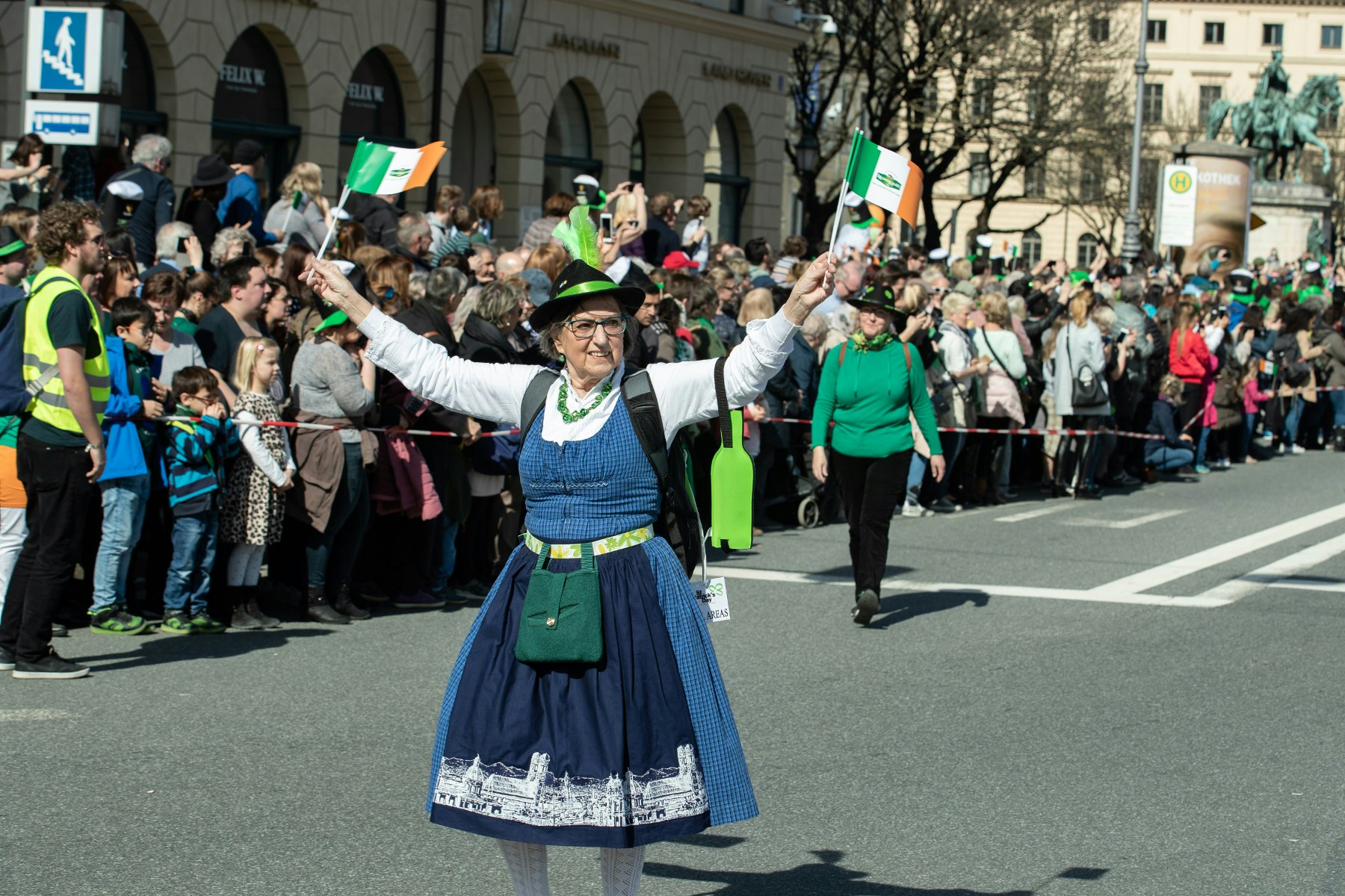 A woman in traditional Bavarian dress walks in Munich's St Patrick's Day parade waving two Irish flags