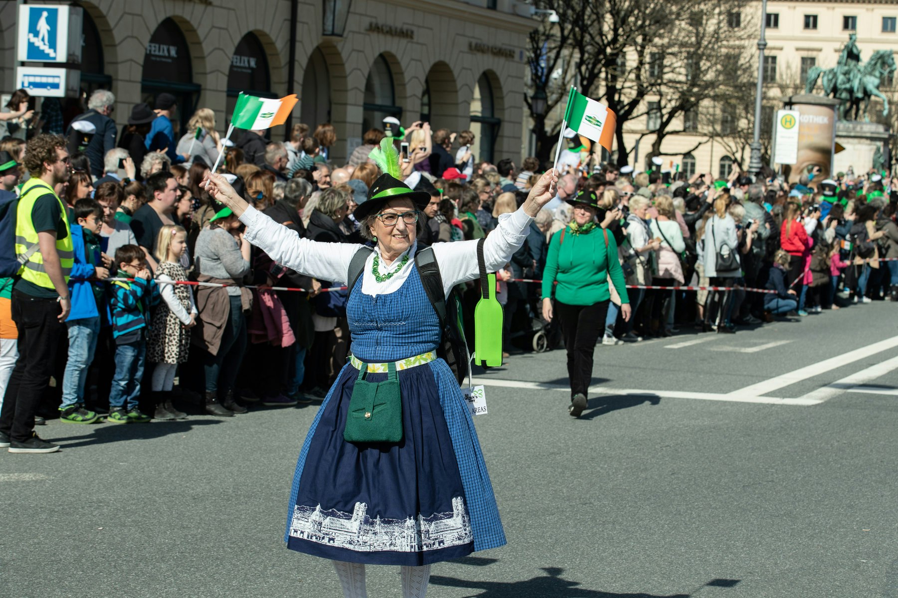 En kvinna i traditionell bayersk klänning går i Münchens St Patrick's Day-parad och viftar med två irländska flaggor