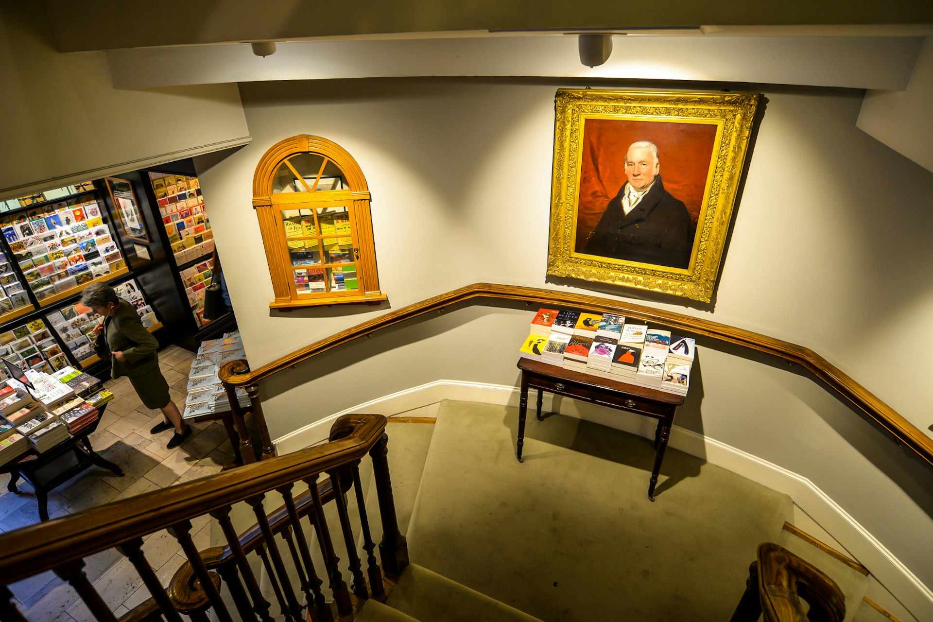 The staircase in Hatchards. A landing in the middle of the staircase has a portrait of a man, with a table of books below it.