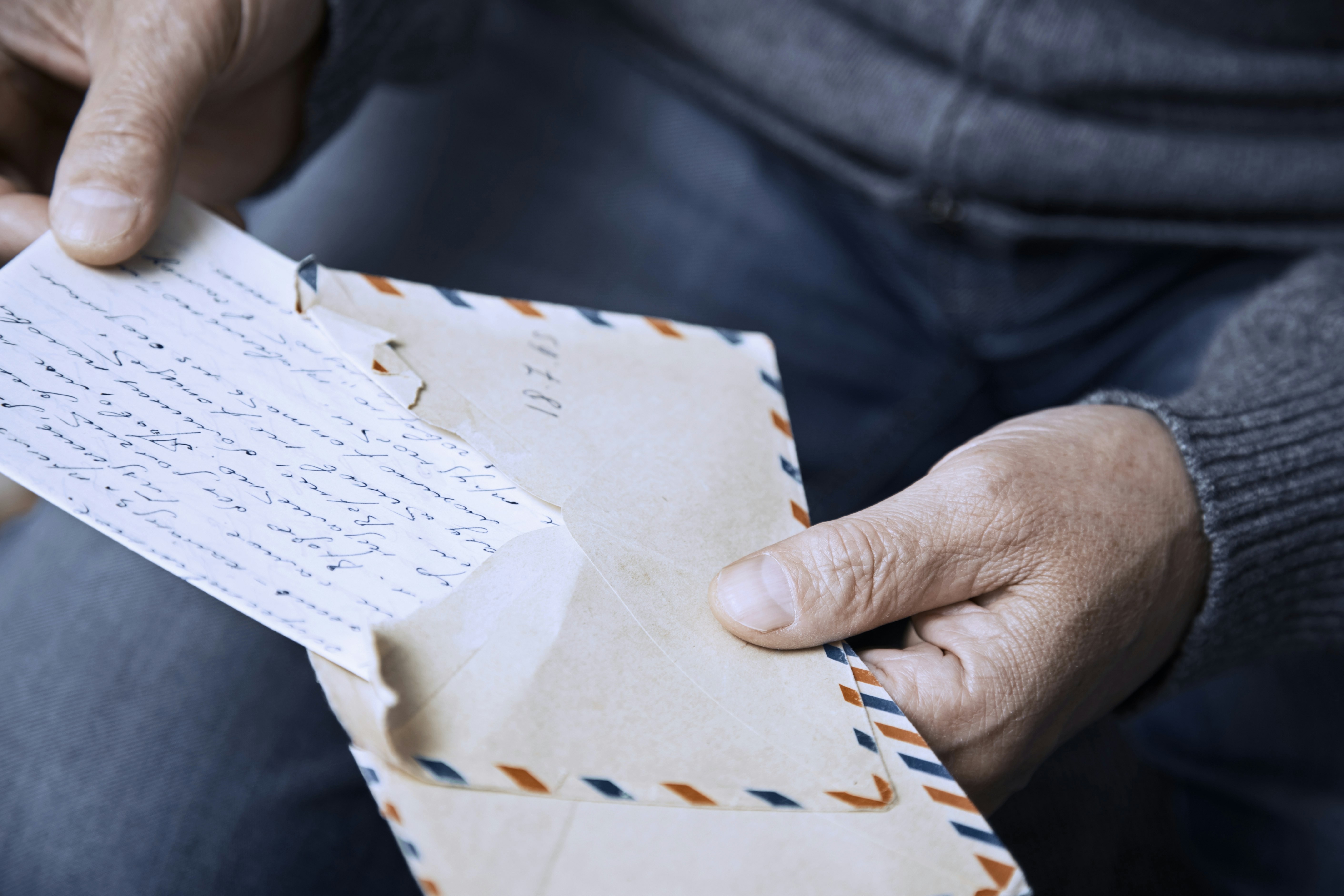 The hands of an elderly man open an envelope and handwritten letter