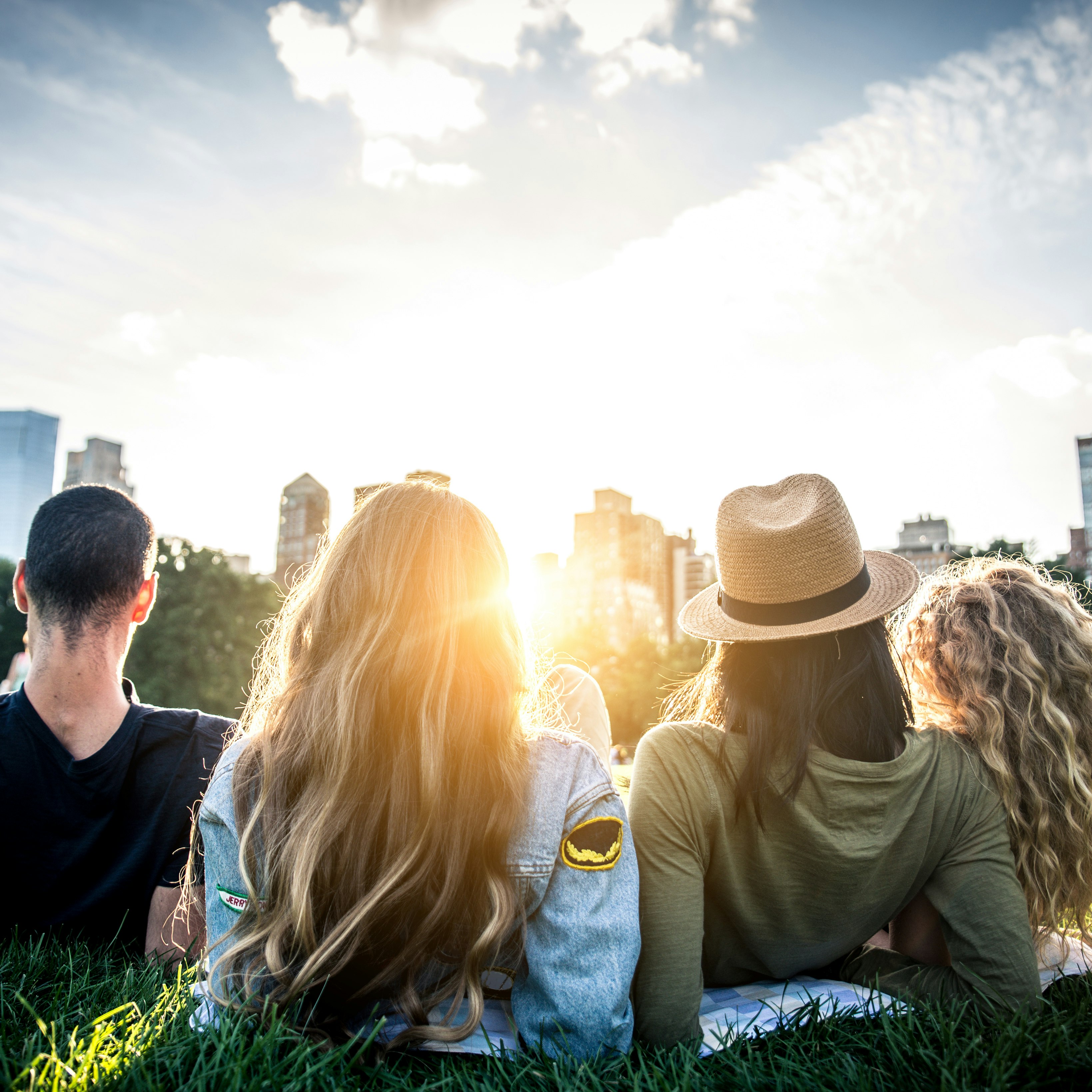 Four people seen from behind, reclining in the grass and looking at the NYC skyline