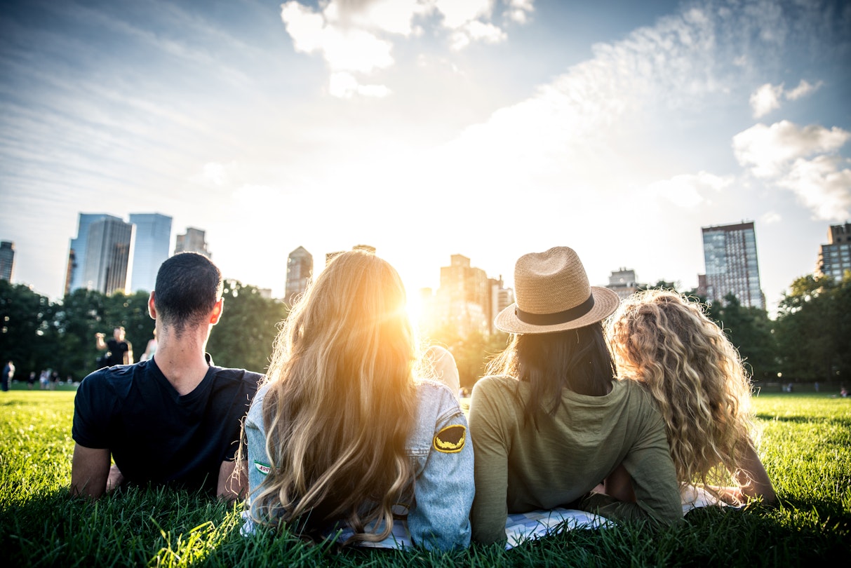 Four people seen from behind, reclining in the grass and looking at the NYC skyline