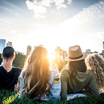 Four people seen from behind, reclining in the grass and looking at the NYC skyline