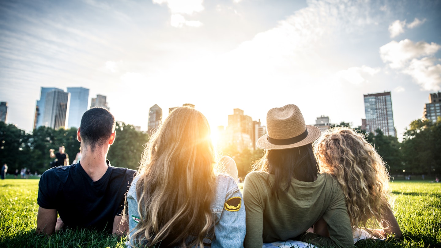 Four people seen from behind, reclining in the grass and looking at the NYC skyline