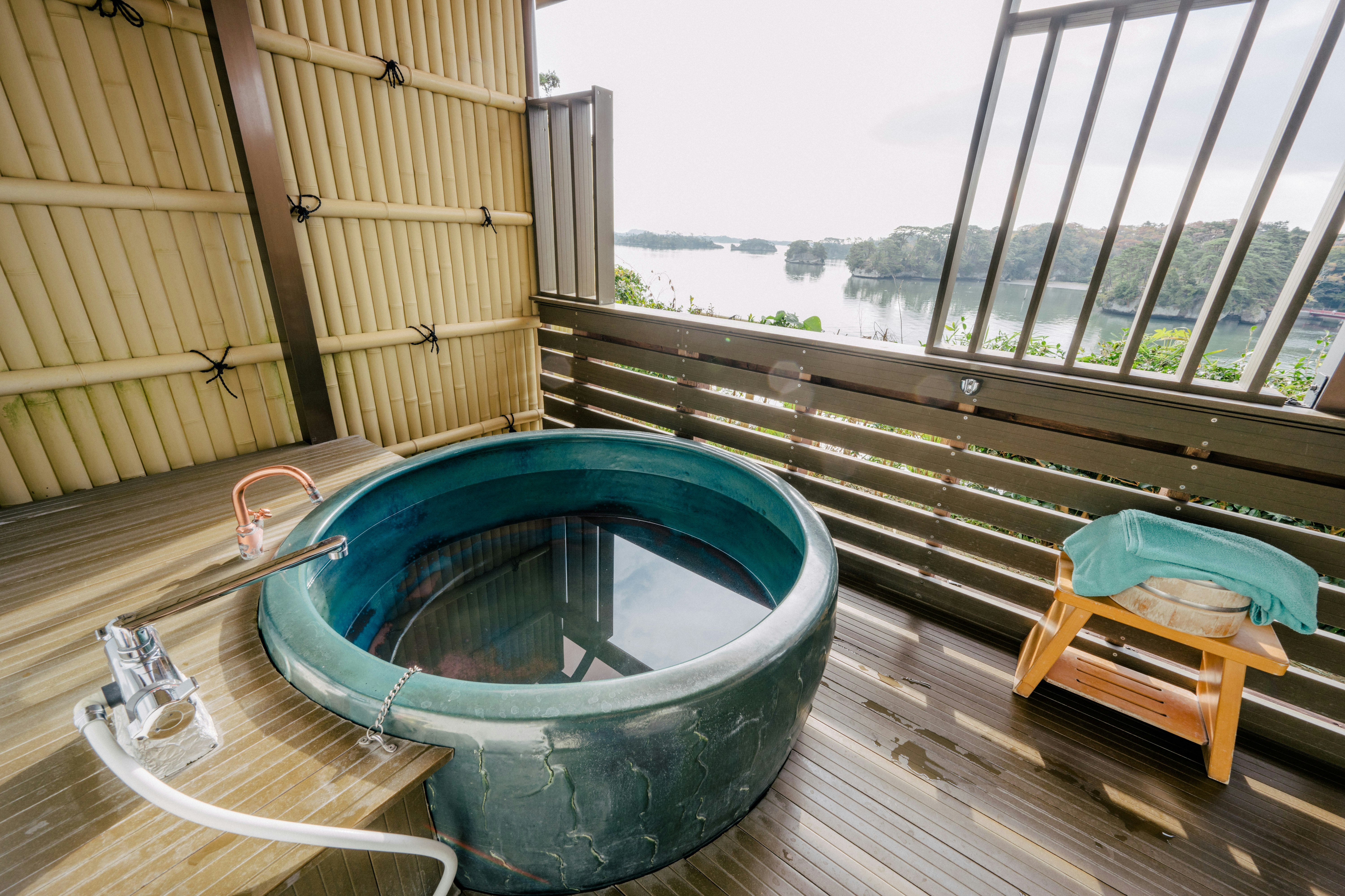 A blue onsen bath on a wooden balcony with views of nature beyond