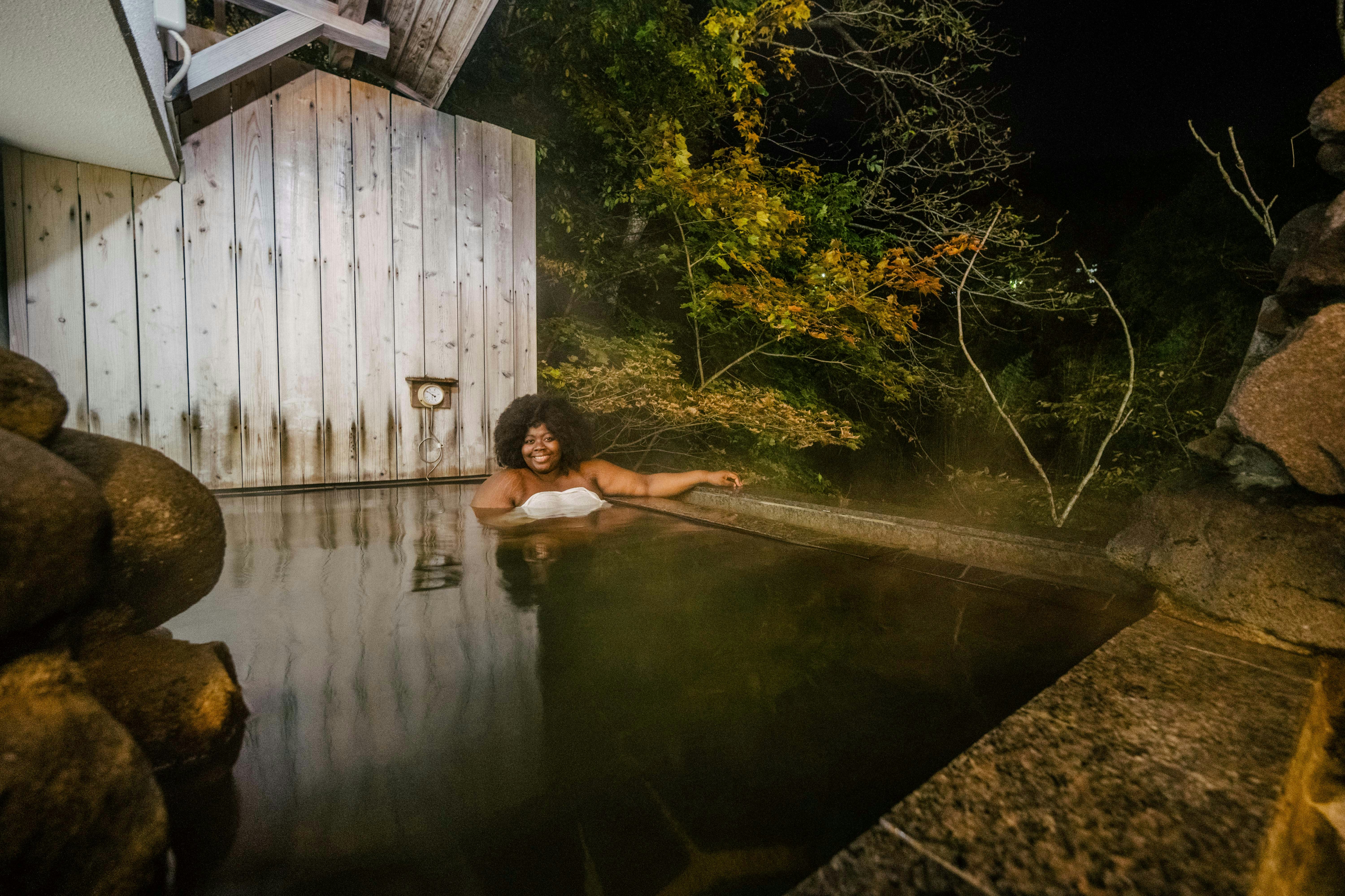 A woman relaxes in an onsen surrounded by nature